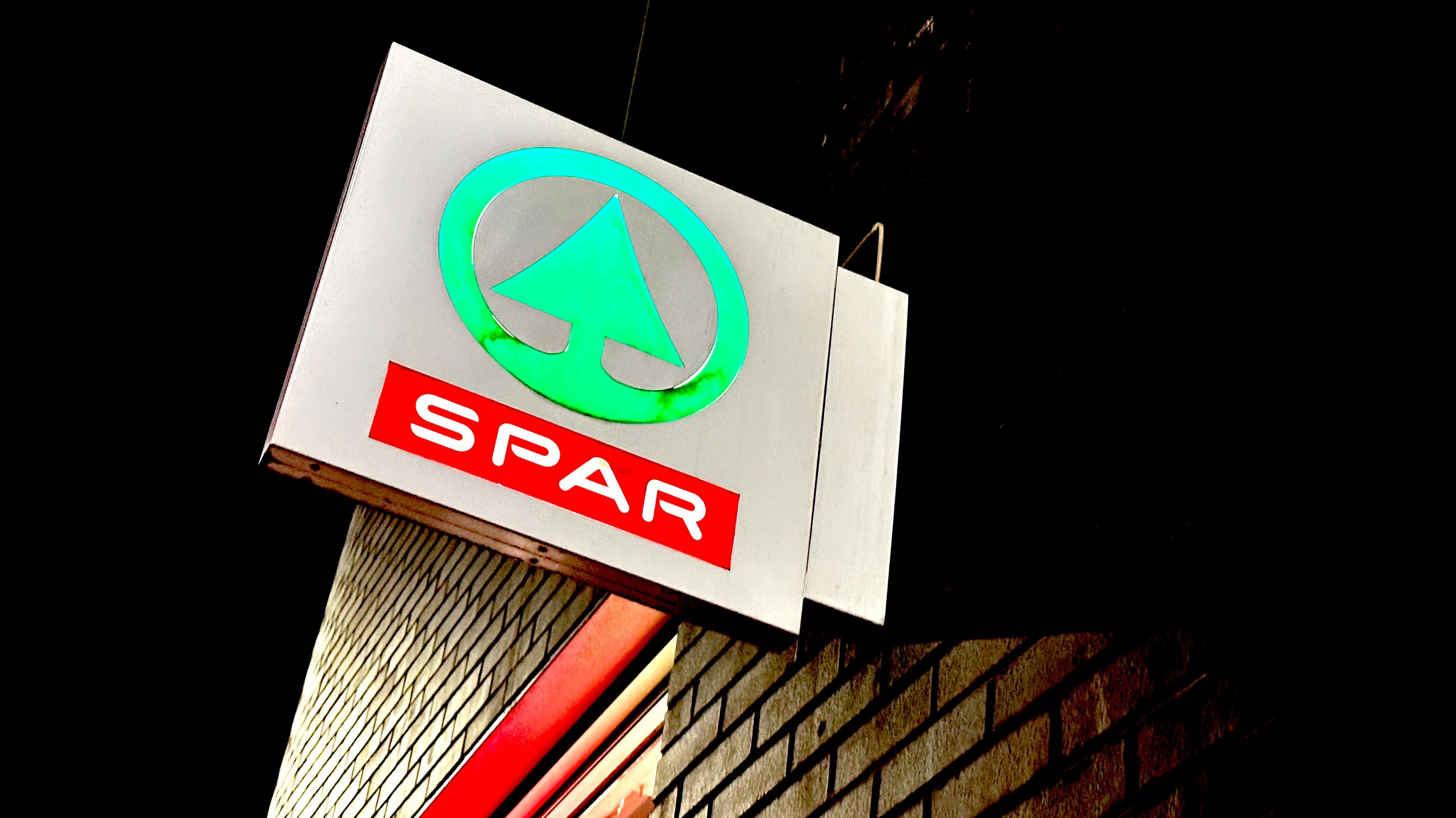 a Spar supermarket outside store sign. It's night and the sign is lit up. The logo is a green tree in a circle.