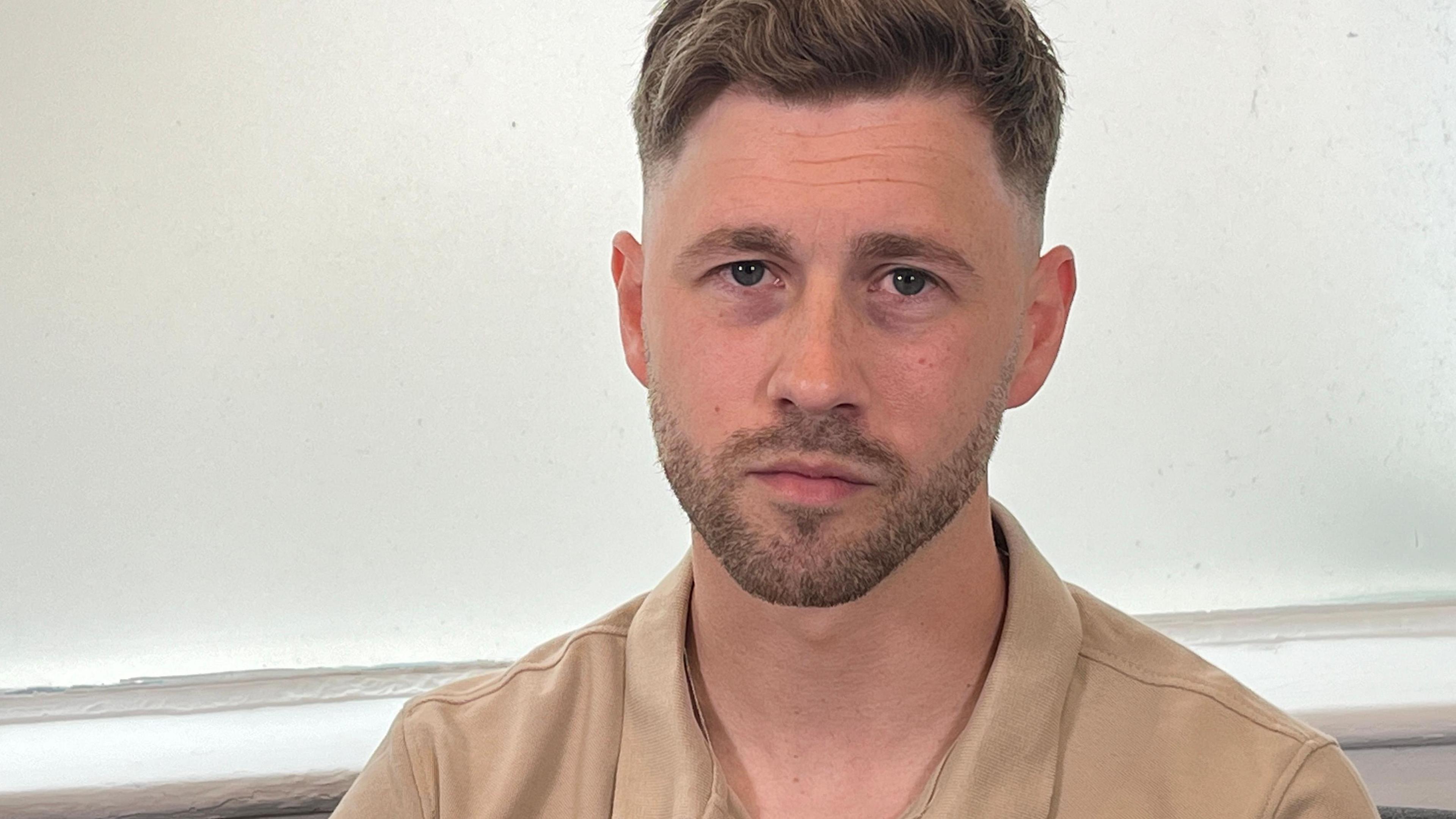 Billy Bashford has short blond hair and a goatee beard. He wears a camel-coloured polo shirt.