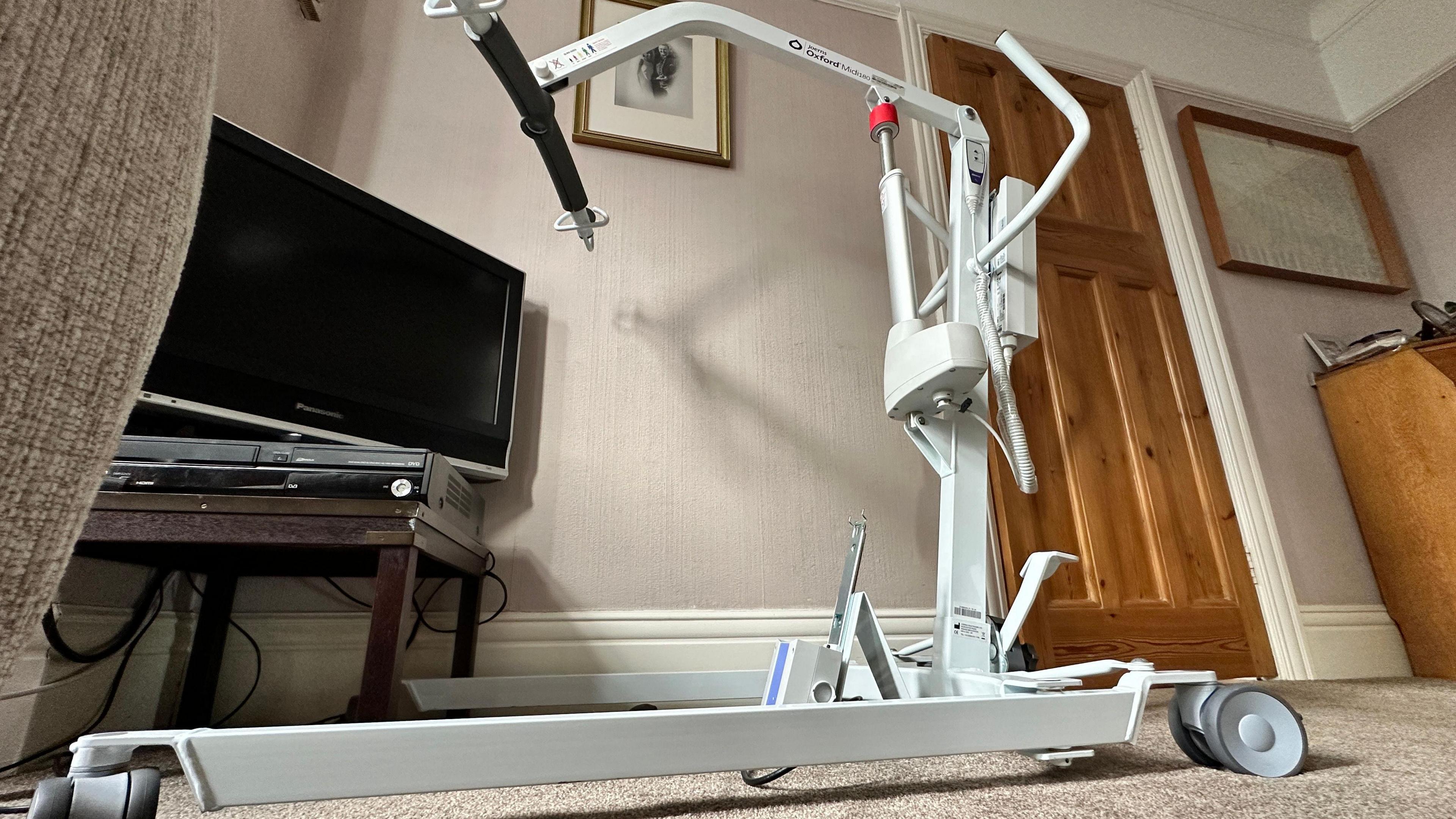 Photo of a hoist, which is a white metal machine operated by electricity and is used to lift people up so they can be moved. The hoist is sitting idle in Eric Watt's front room. 