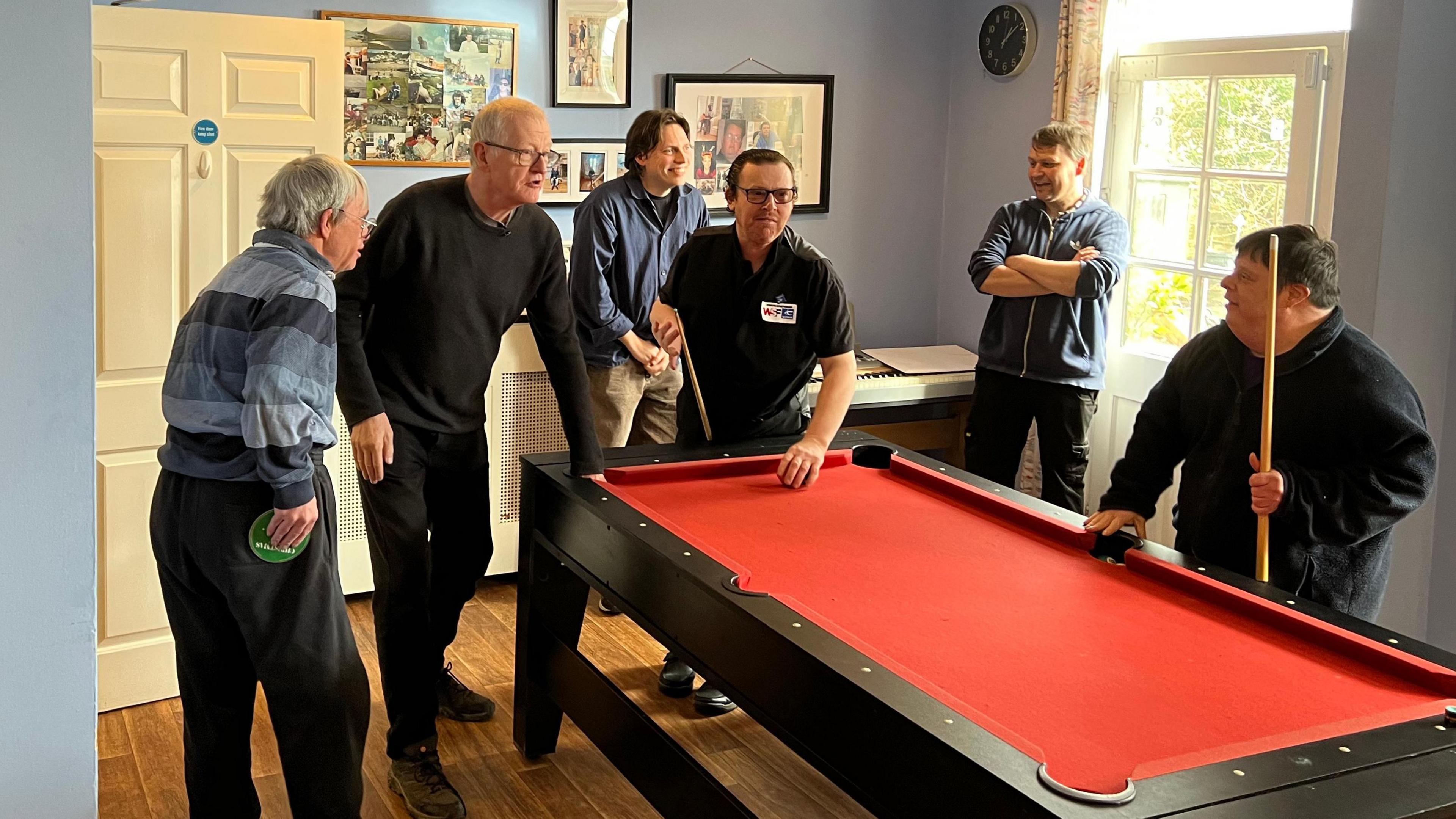 A group of six men standing around a pool table. Steve Davis, Adrian and Paul are in the picture with three other men. None of them are looking at the camera. 