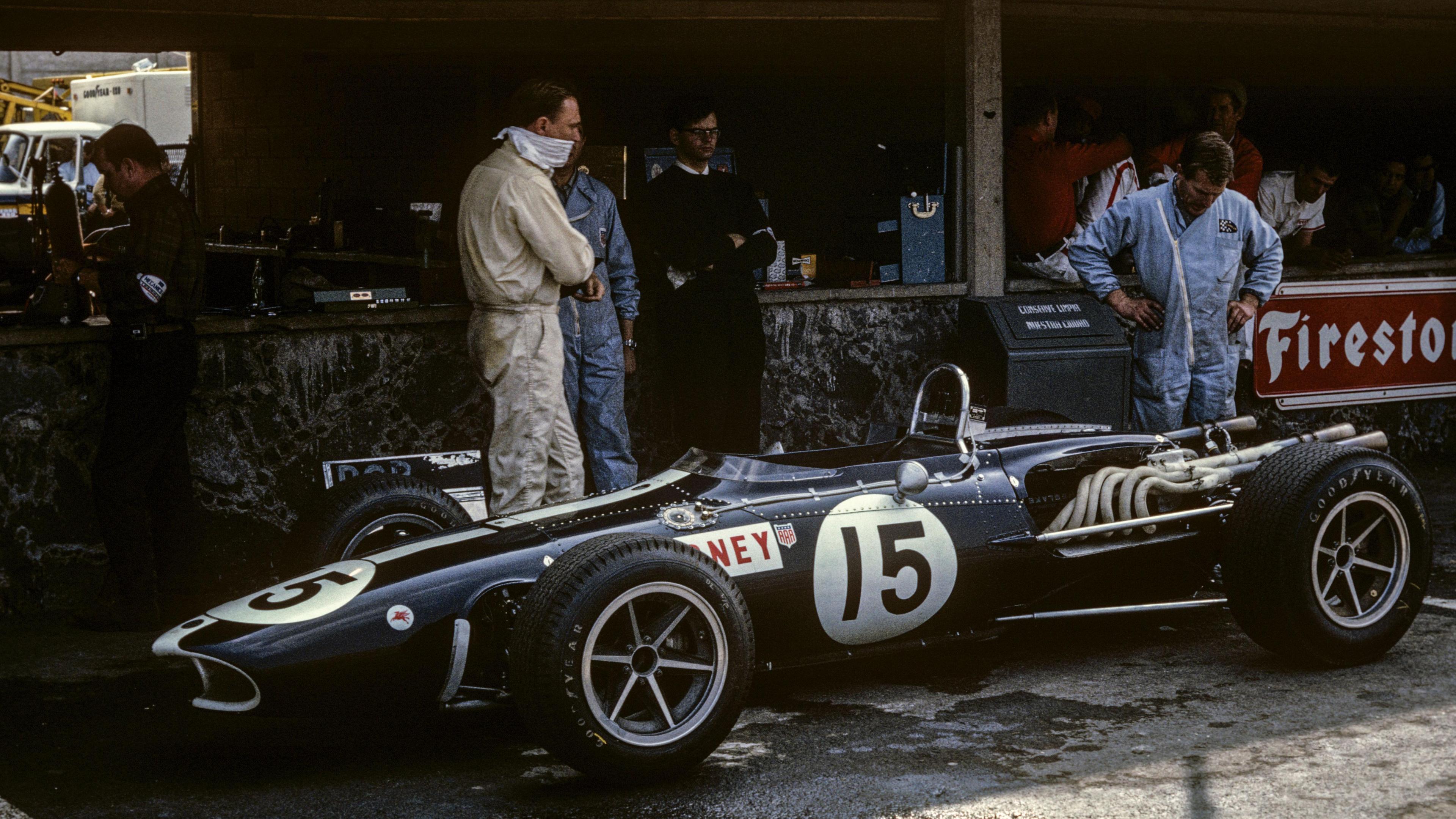 Dan Gurney stood looking over his Eagle Mk1 car in the pits at the 1966 Mexican Grand Prix