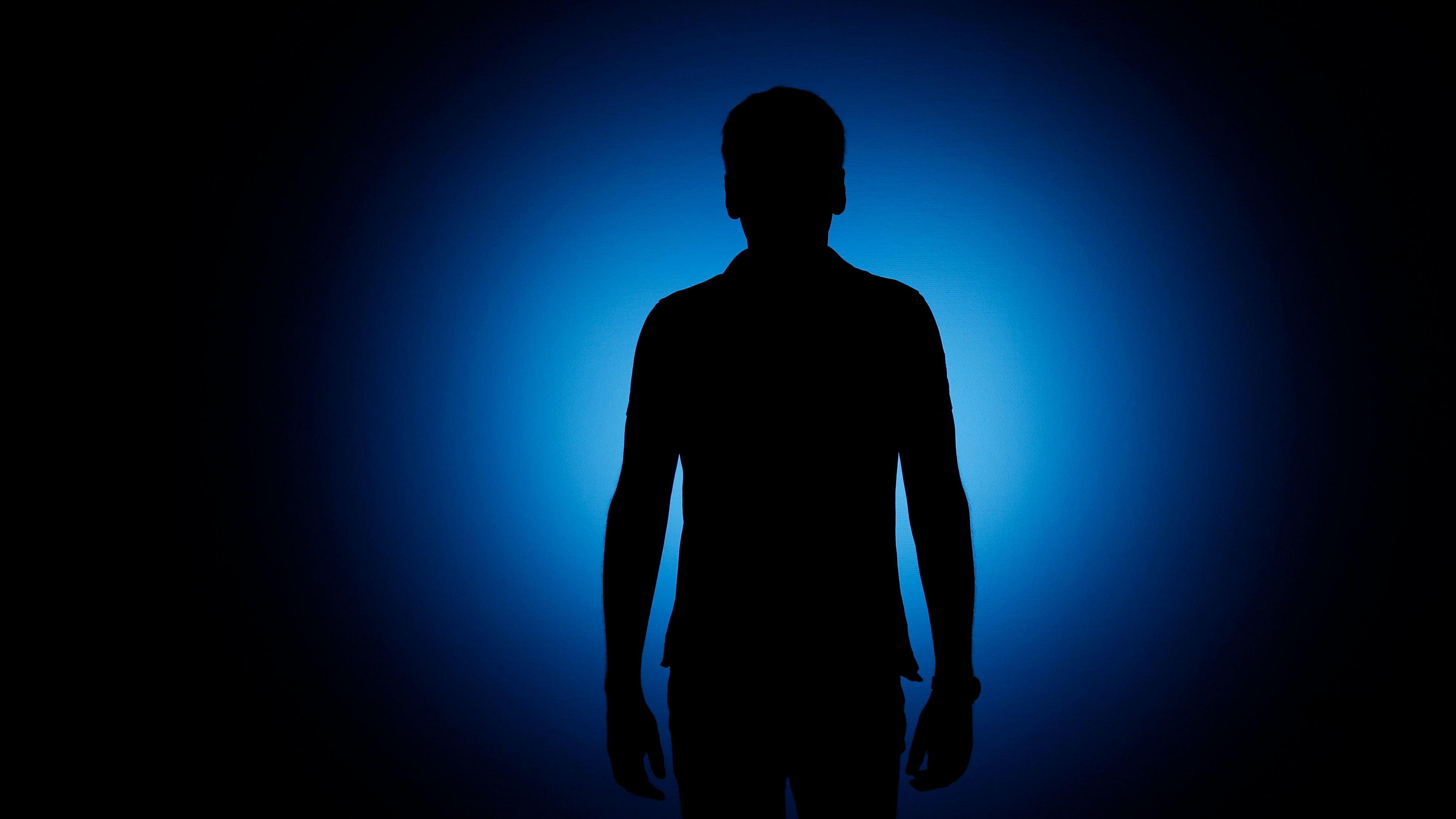 Silhouette of a man standing in front of a blue background.