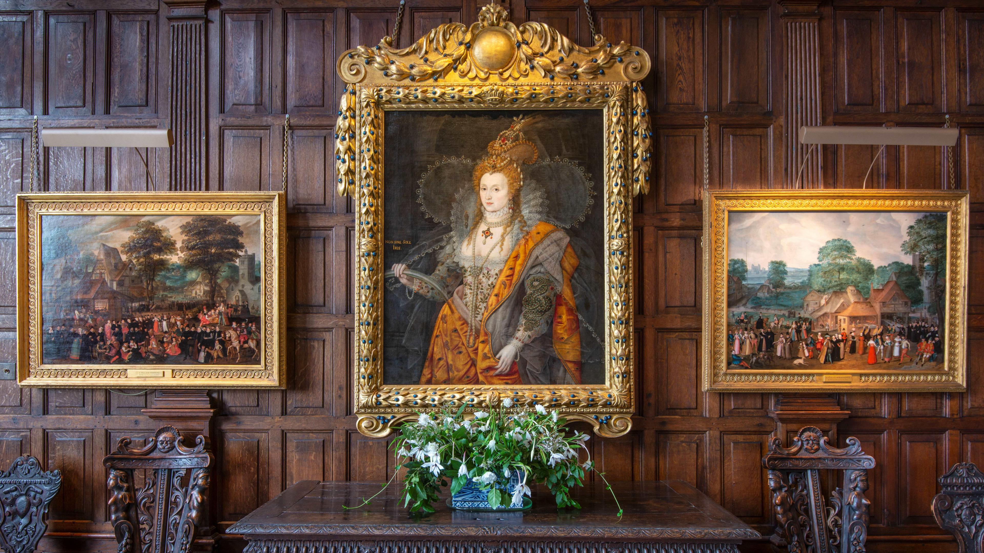 Three pictures on a wooden panelled room, by a flower arrangement and four chairs, in a room in Hatfield House