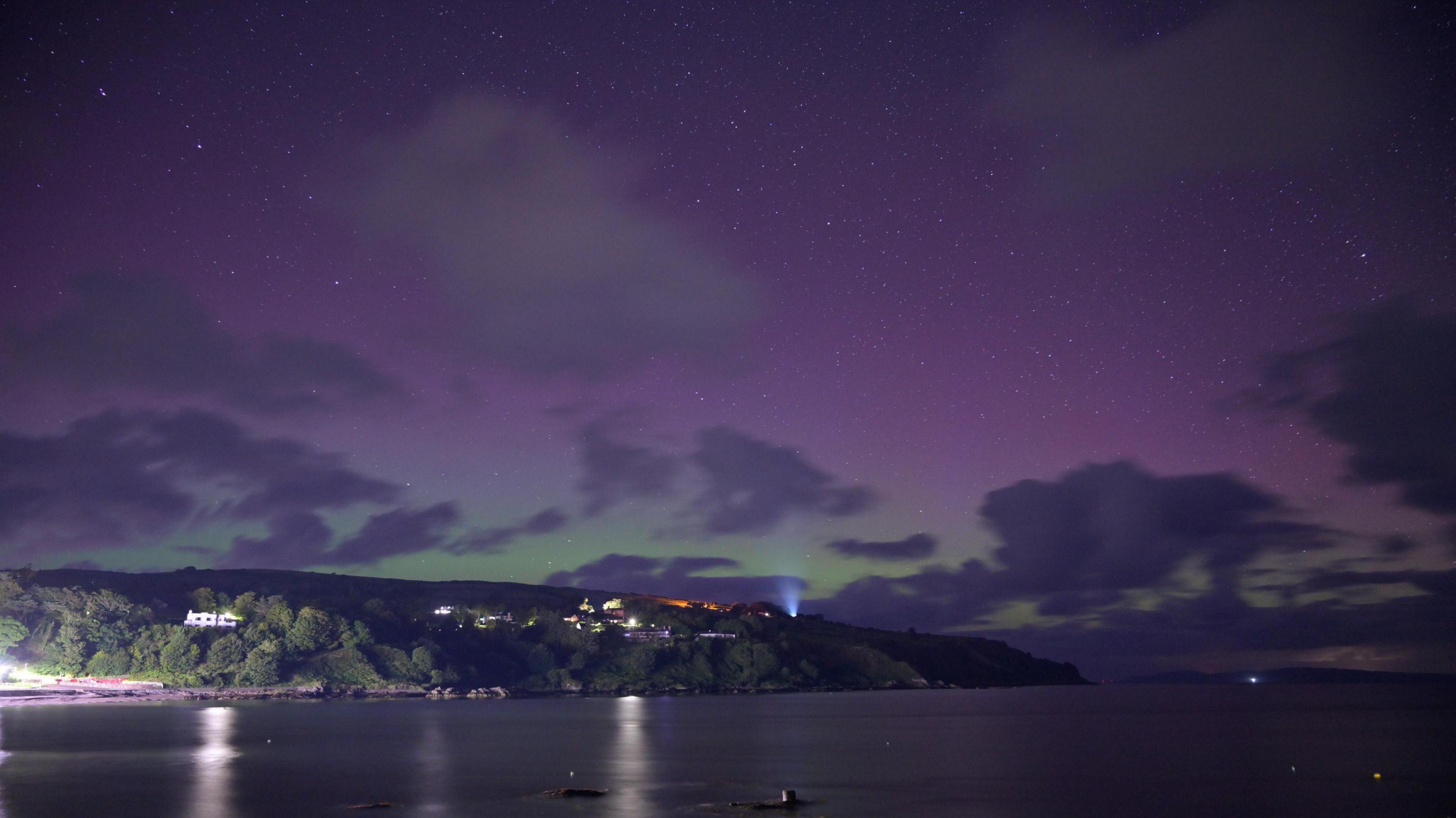 Hills sit to the right of a cove, a purple green glow from the northern lights dominates the top half of the frame