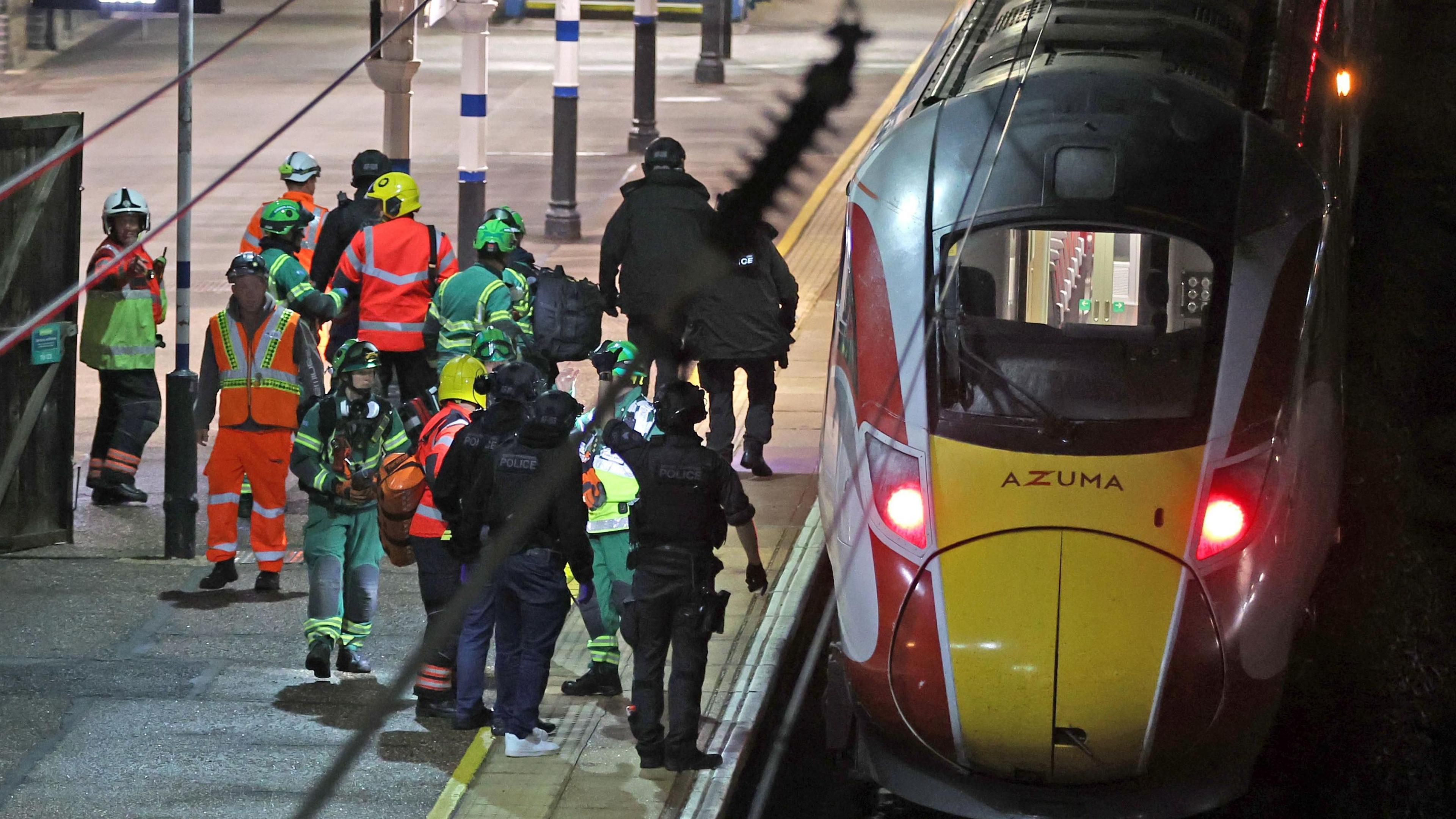 A crowd of emergency services personnel on a railway station platform at Huntingdon railway station standing by a stationary LNER train.