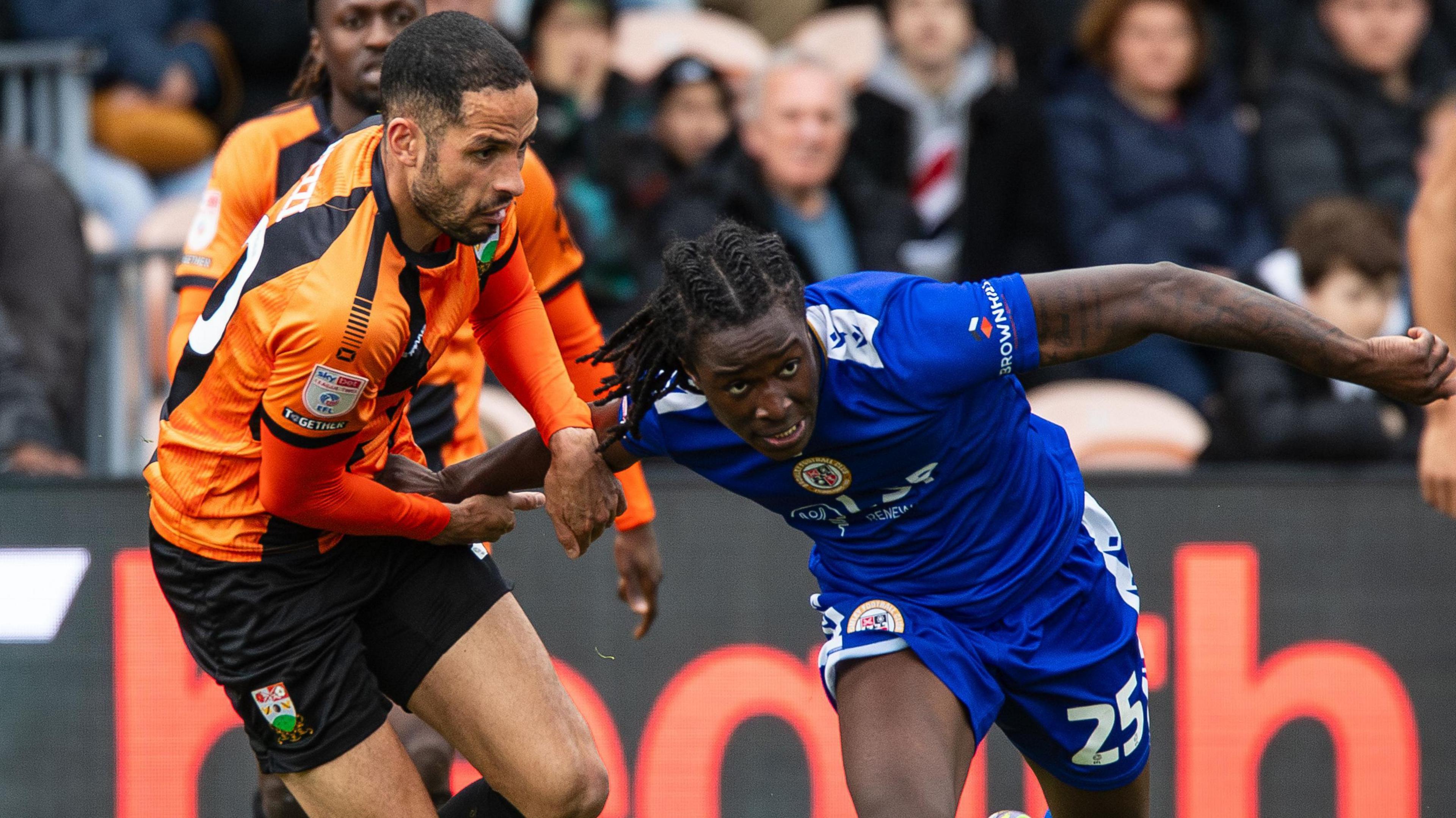 Joe Kizzi in Barnet's amber and black kit grapples with an attacker in all blue