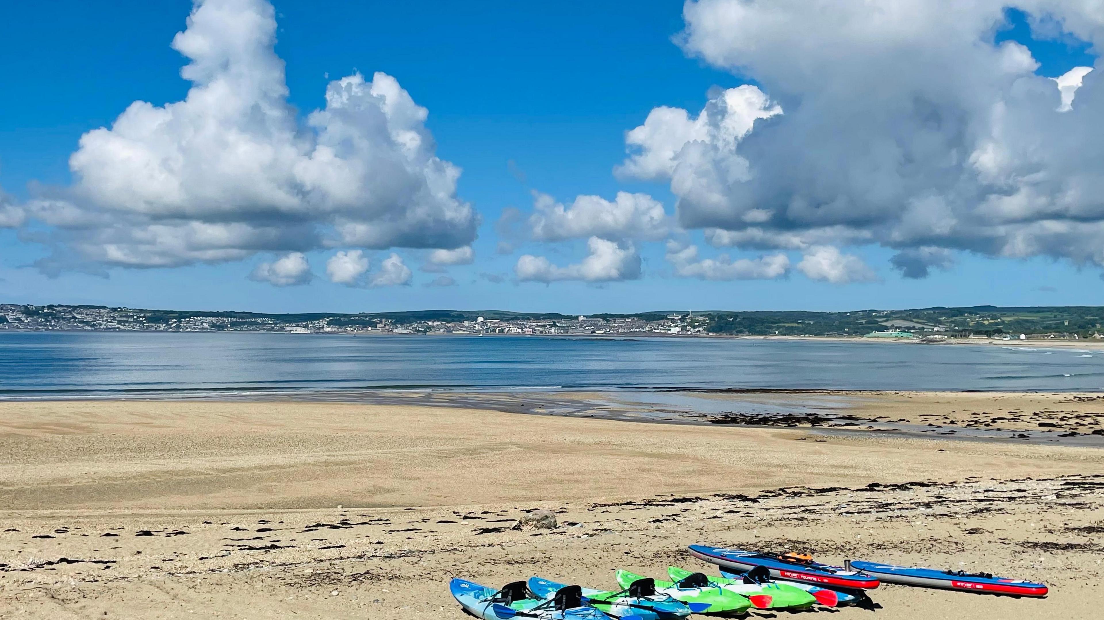 Coastal view with paddleboards on a beach. Blue skies and fluffy clouds are overhead