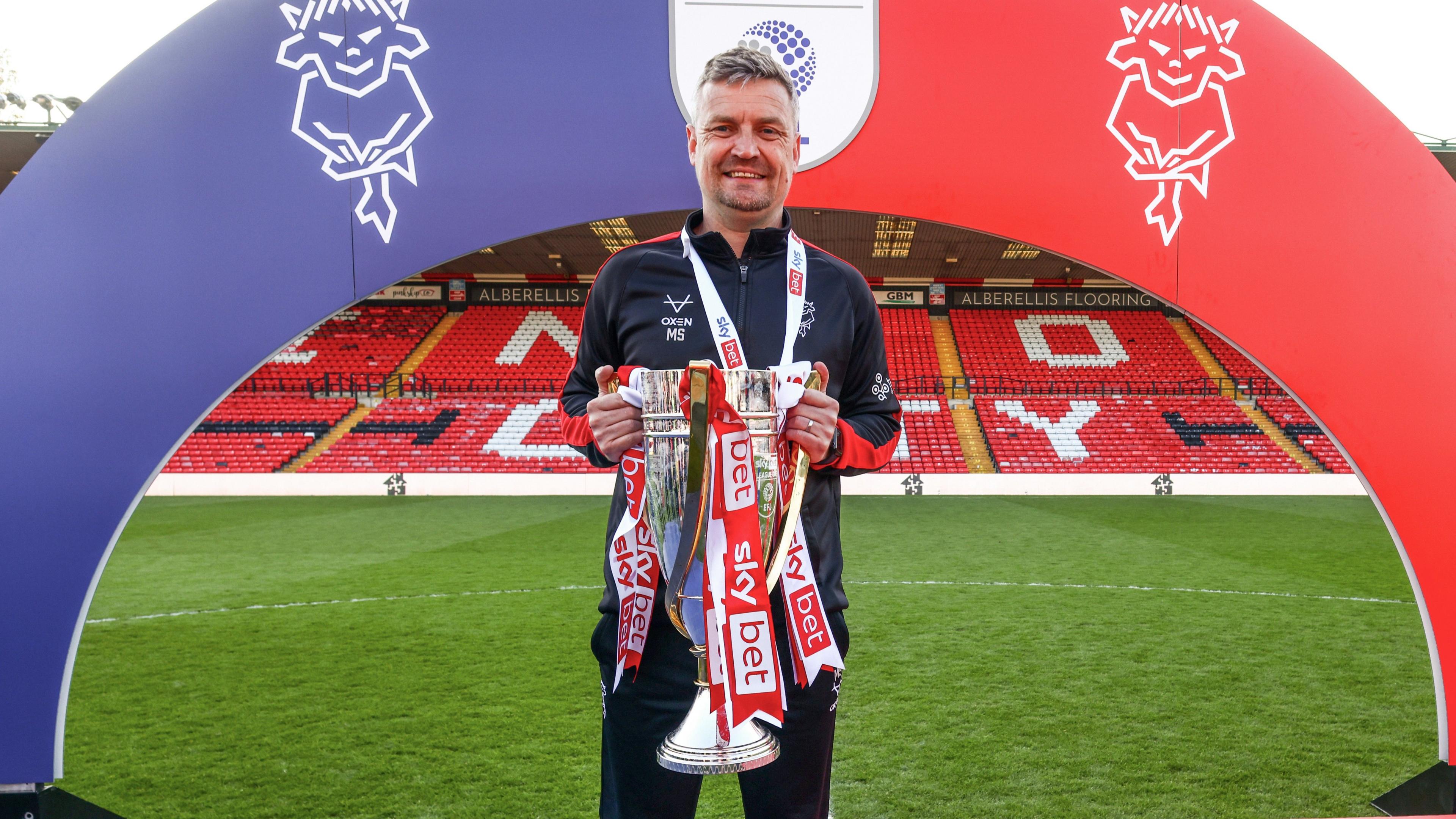 Former Lincoln City manager Michael Skubala poses with the League One champions trophy on the pitch at Sincil Bank at the end of the 2025-26 season.