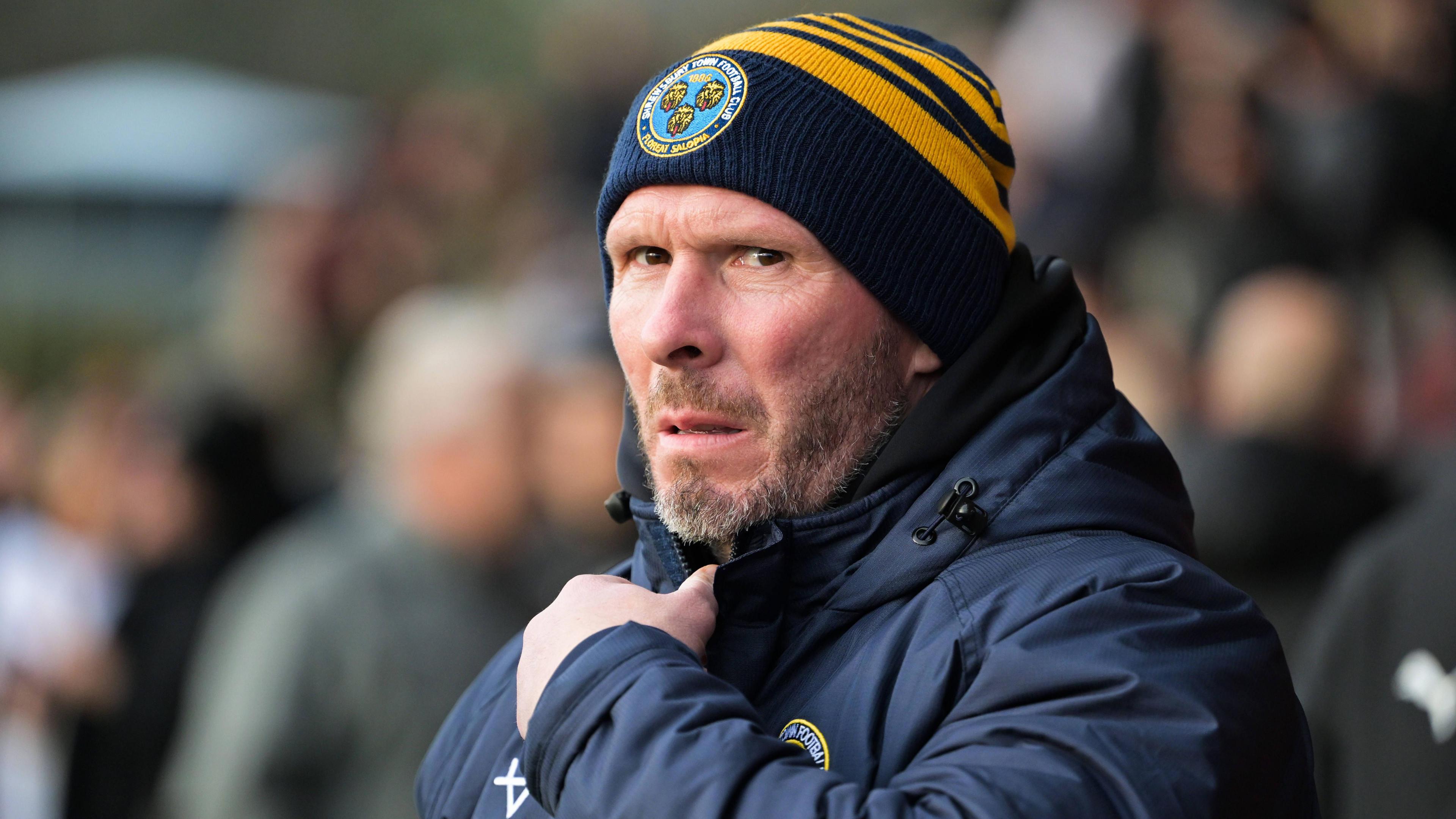 Shrewsbury Town manager Michael Appleton in his club beanie and puffer coat watches on from the touchline