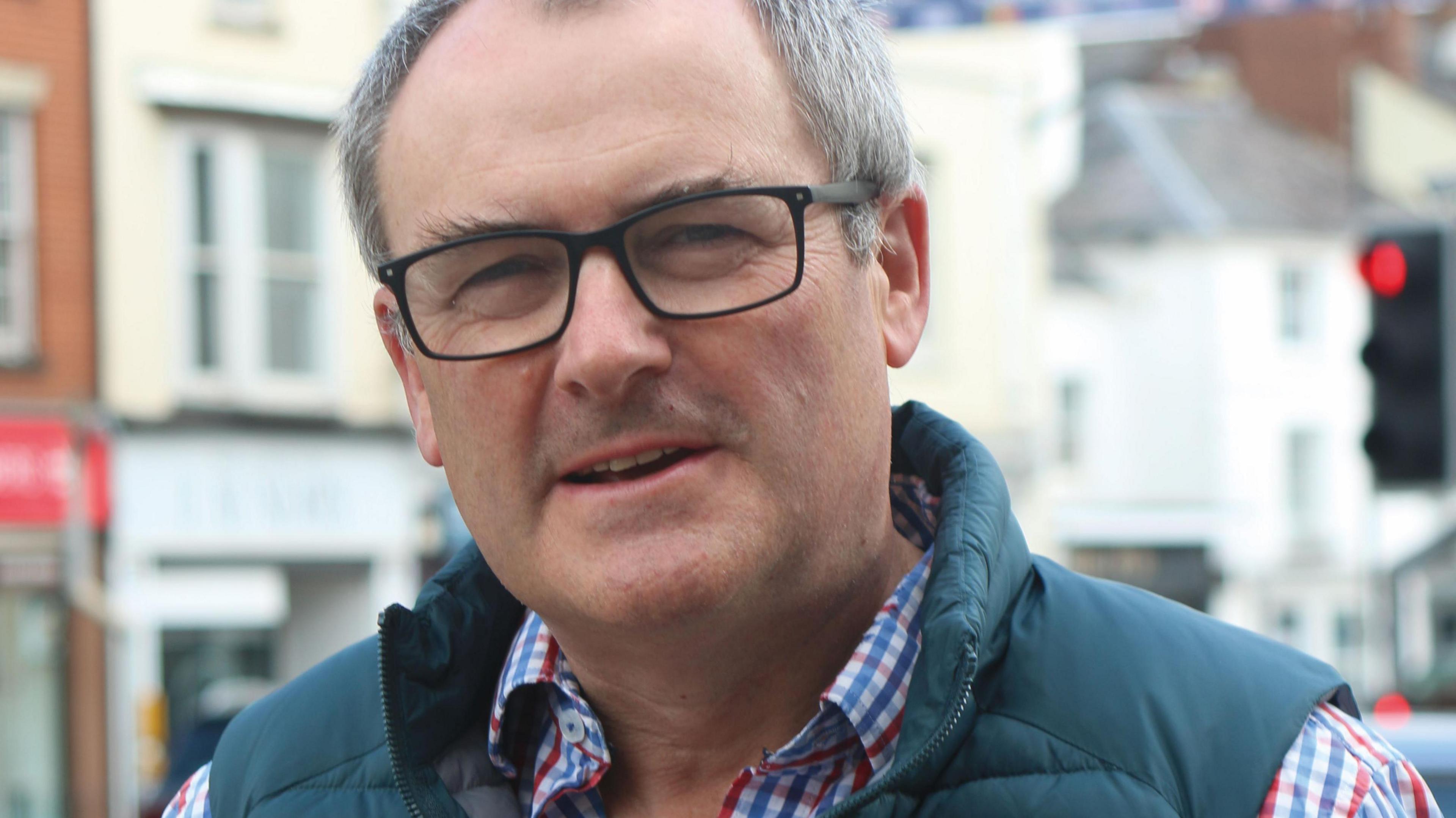 Charles Hansard with black square glasses standing on a high street