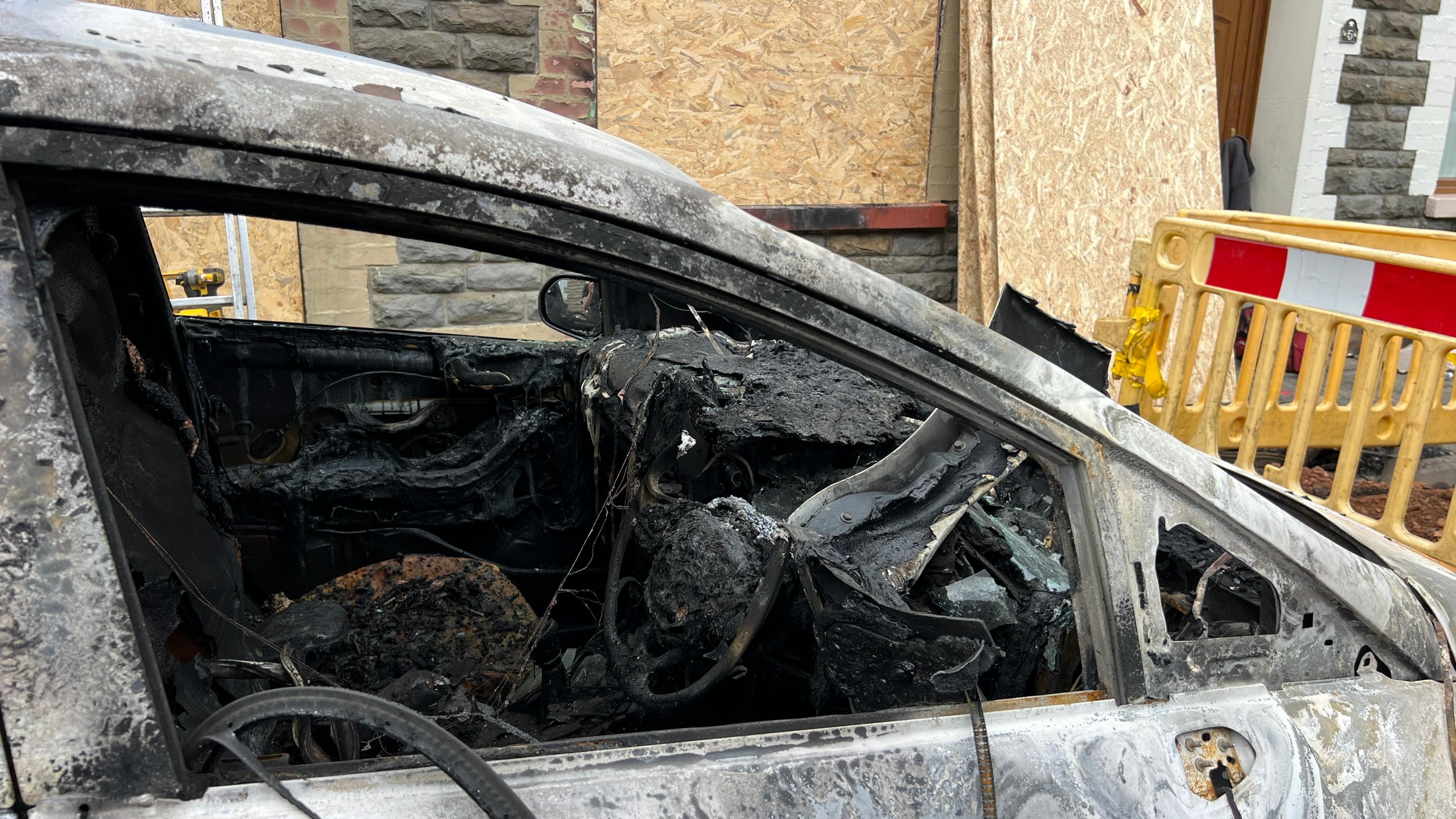 Picture of a burnt out vehicle outside the house the day after the fire. All the glass windows have smashed and the steering wheel and interiors melted down in the heat of the flames.
