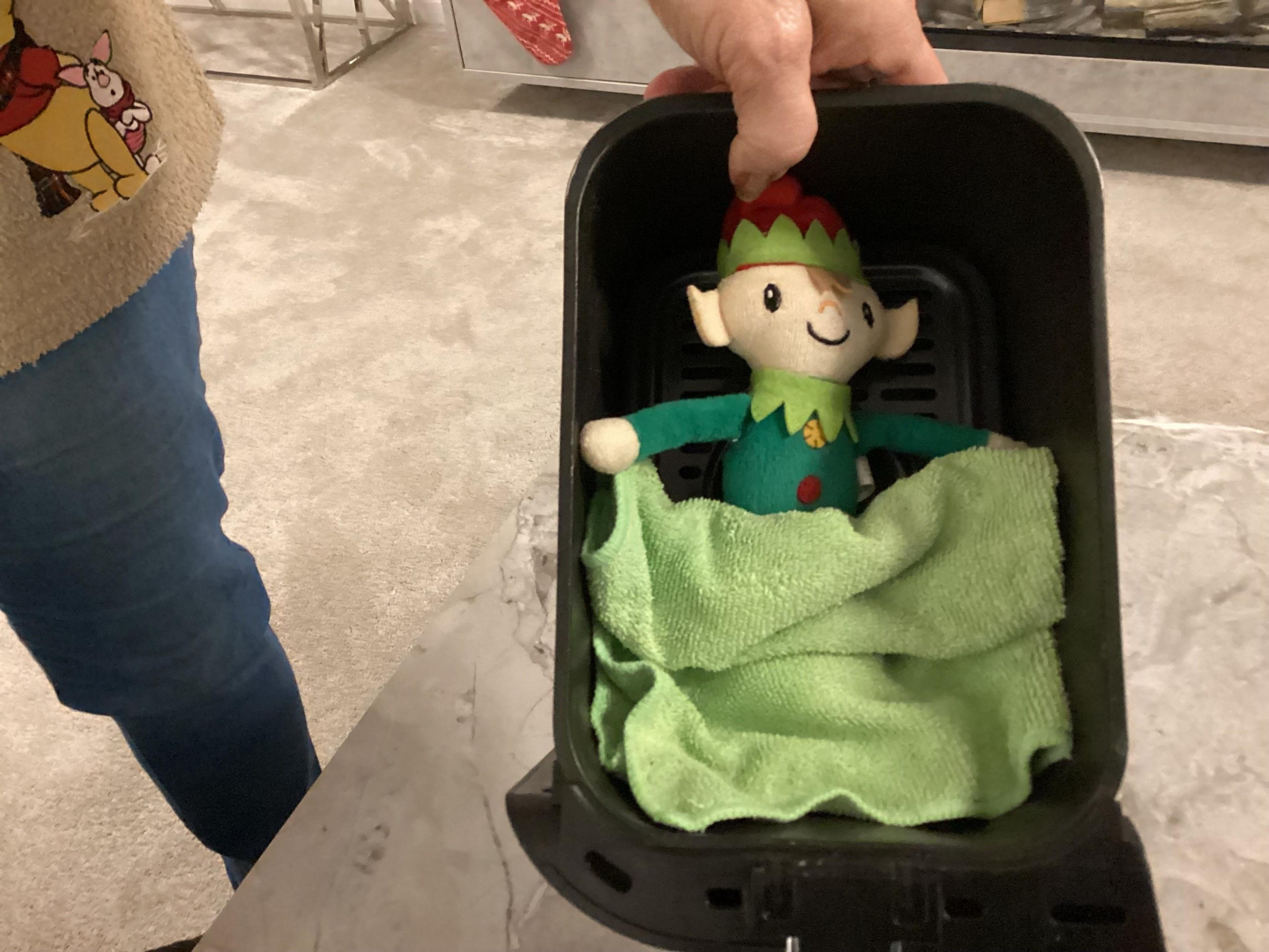 An elf in the air fryer with a cloth as a blanket