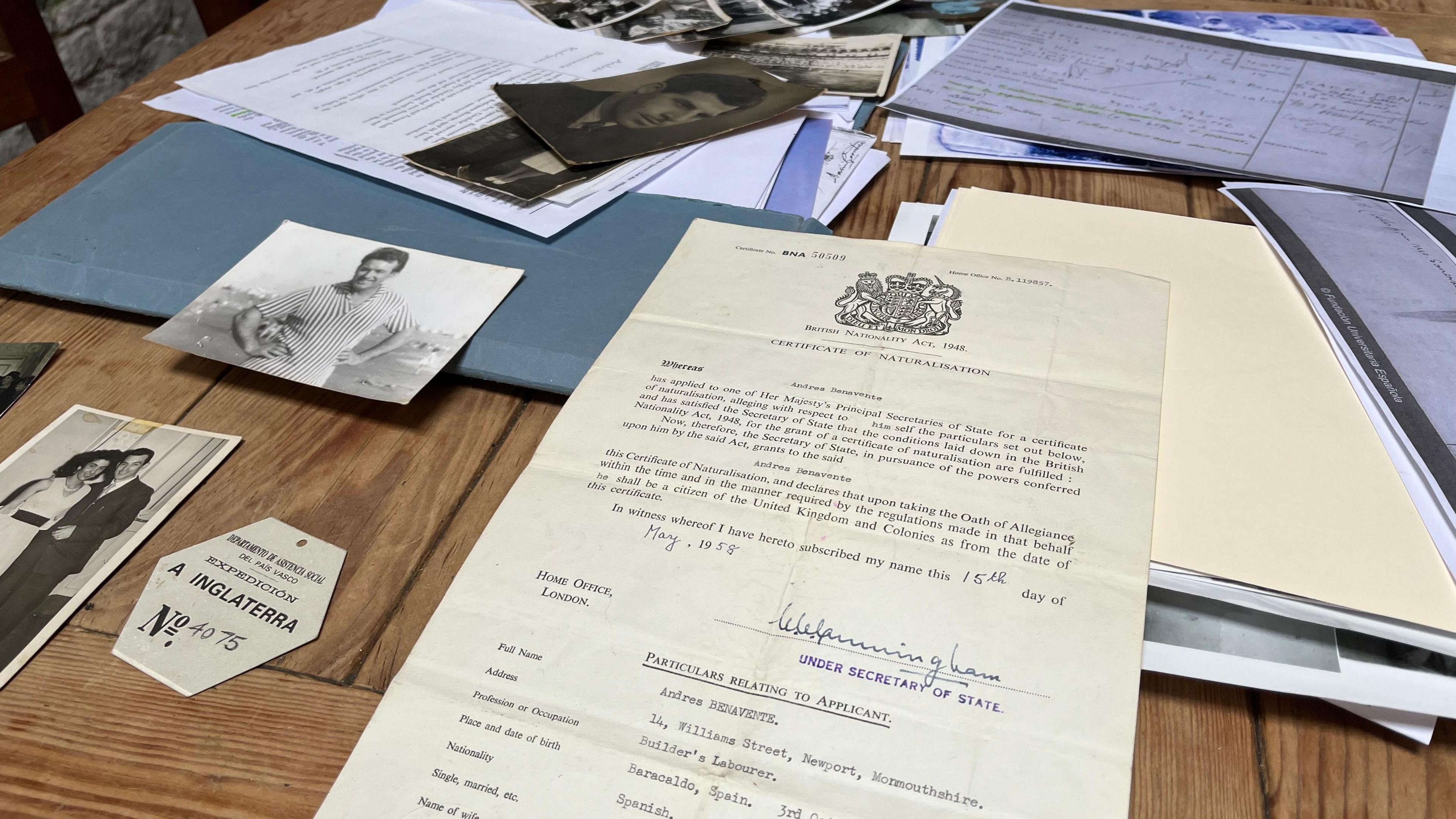 Andres Benavente's naturalisation papers on a table. There are various black and white photos of him on the table as well as other paperwork.