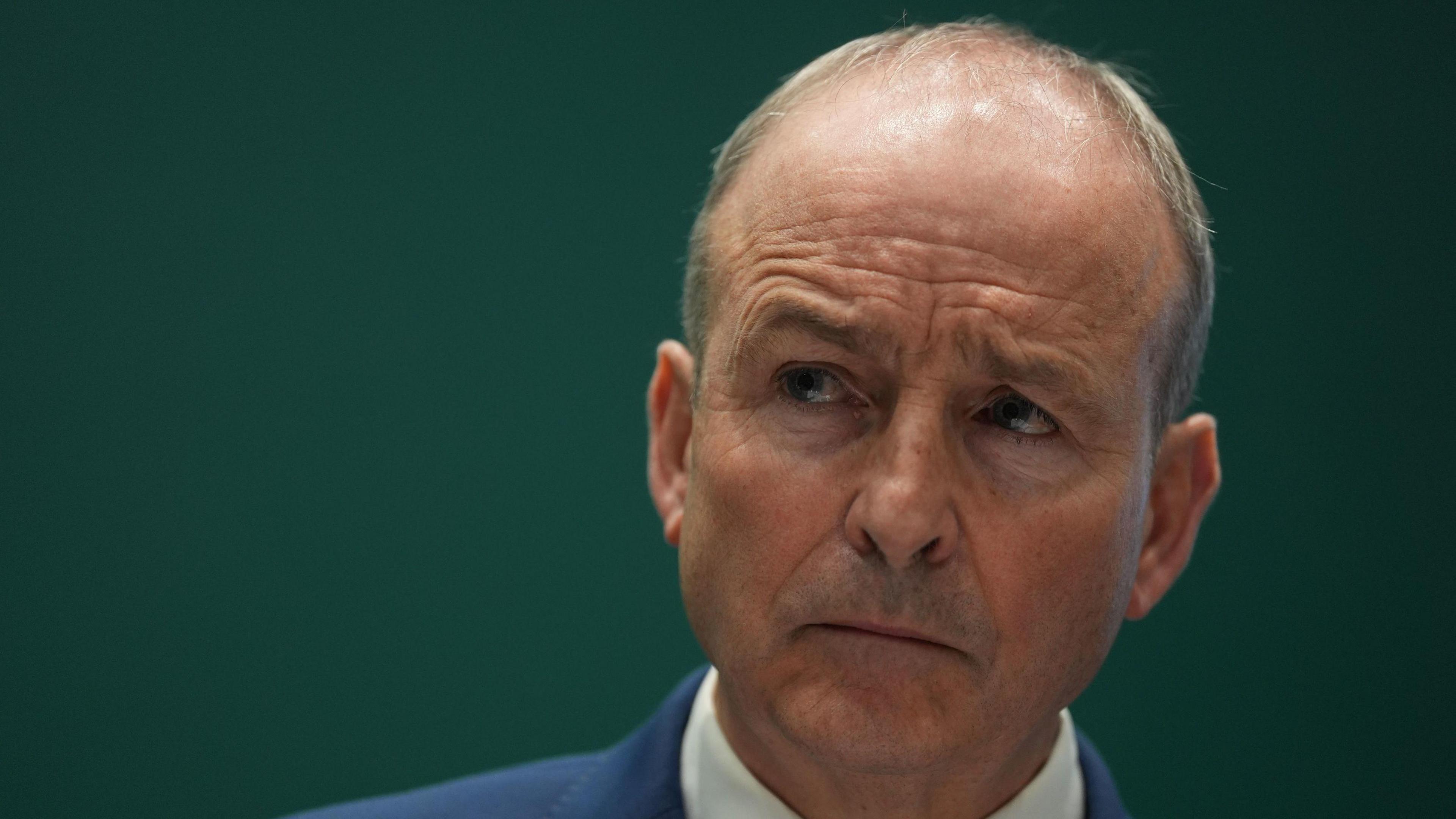 Michael Martin has short grey hair and is frowning in the image as he wears a blue suit jacket and white shirt.