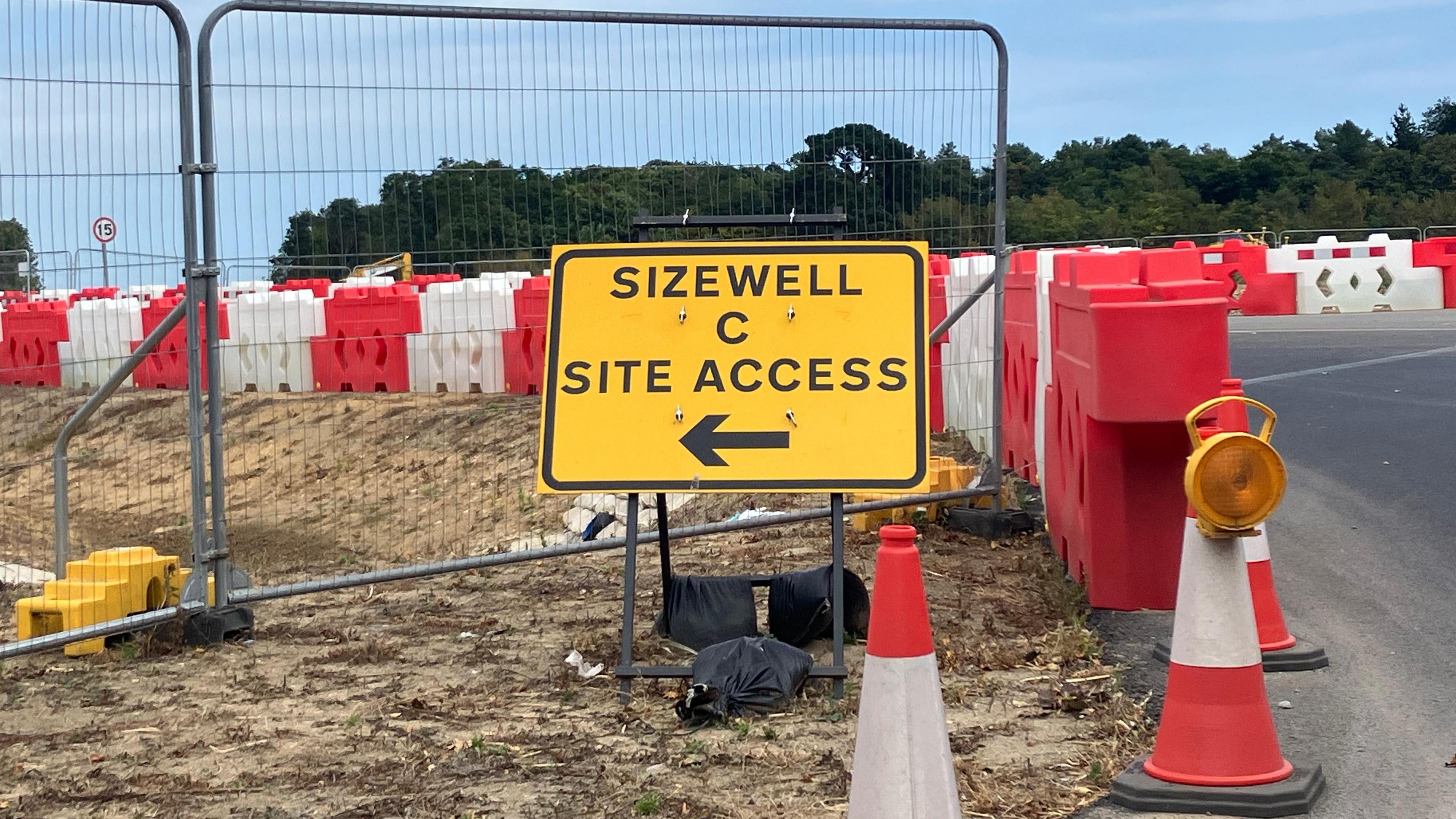 Yellow road sign pointing to Sizewell C site access behind three red and white cones 