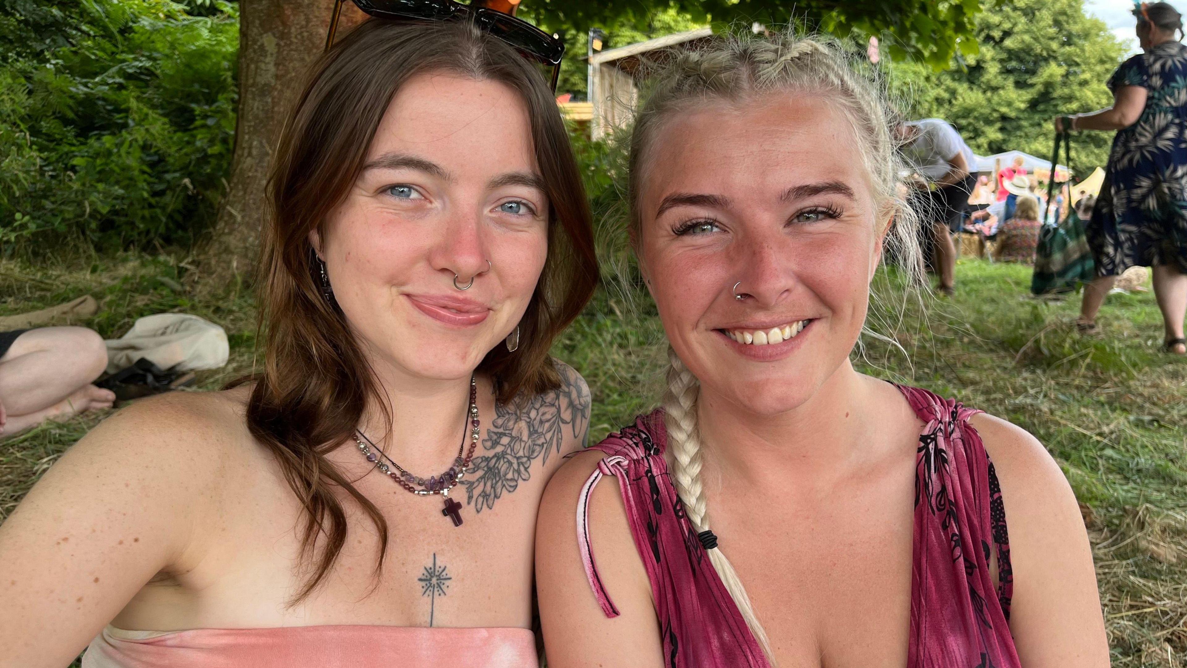 Smiling Megan and Charlotte look directly at the camera, while sitting beside a tree