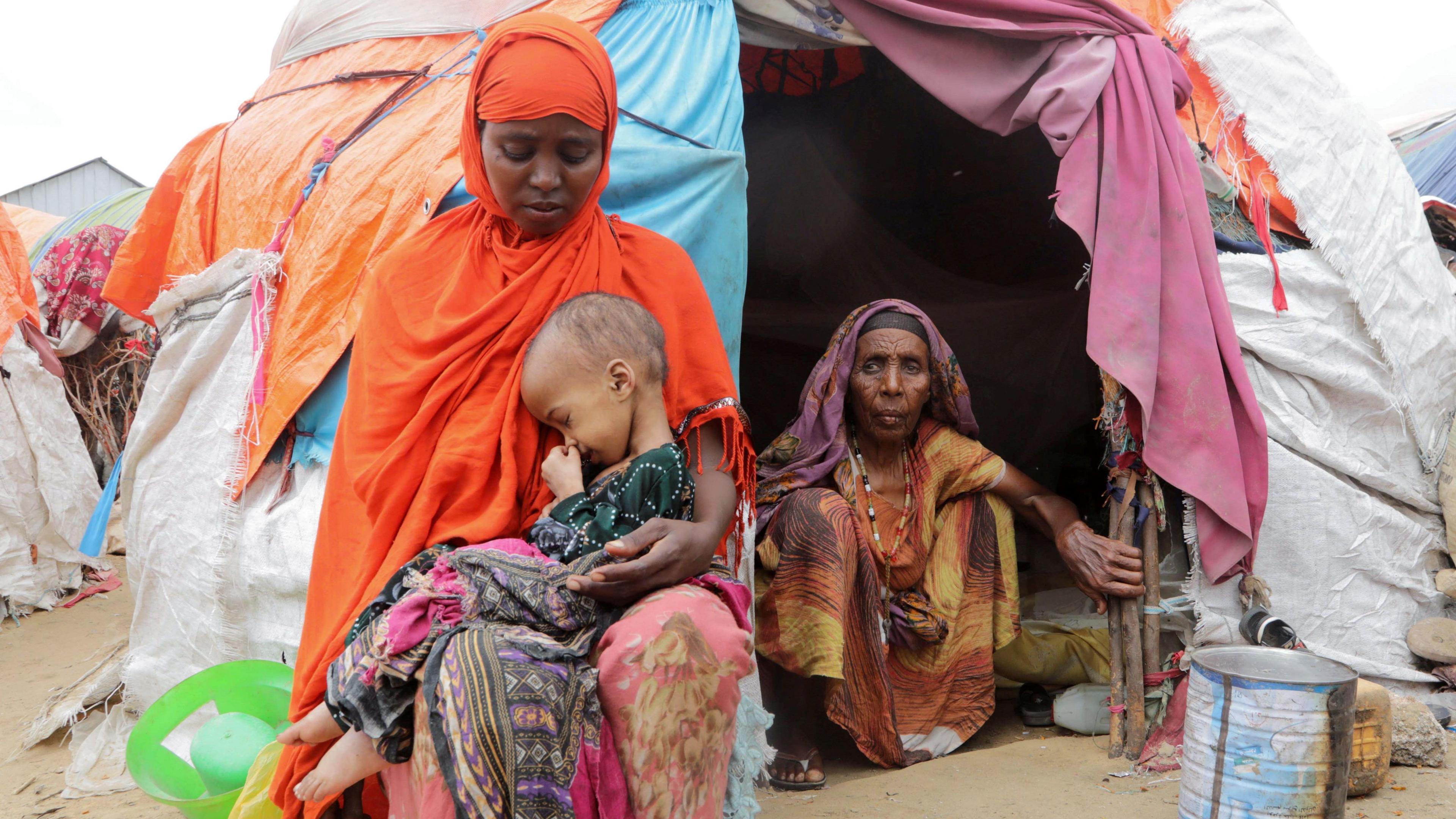 Buney Aayow Ibrahim, a Somali woman affected by the worsening drought due to failed rainy seasons, holds her three-year-old child Sadia Salas Abdi as her grandmother Habiba Osman looks on, next to their makeshift shelter at the Alla Futo camp for internally displaced people, outside the Somalian capital Mogadishu on 23 September 2022.