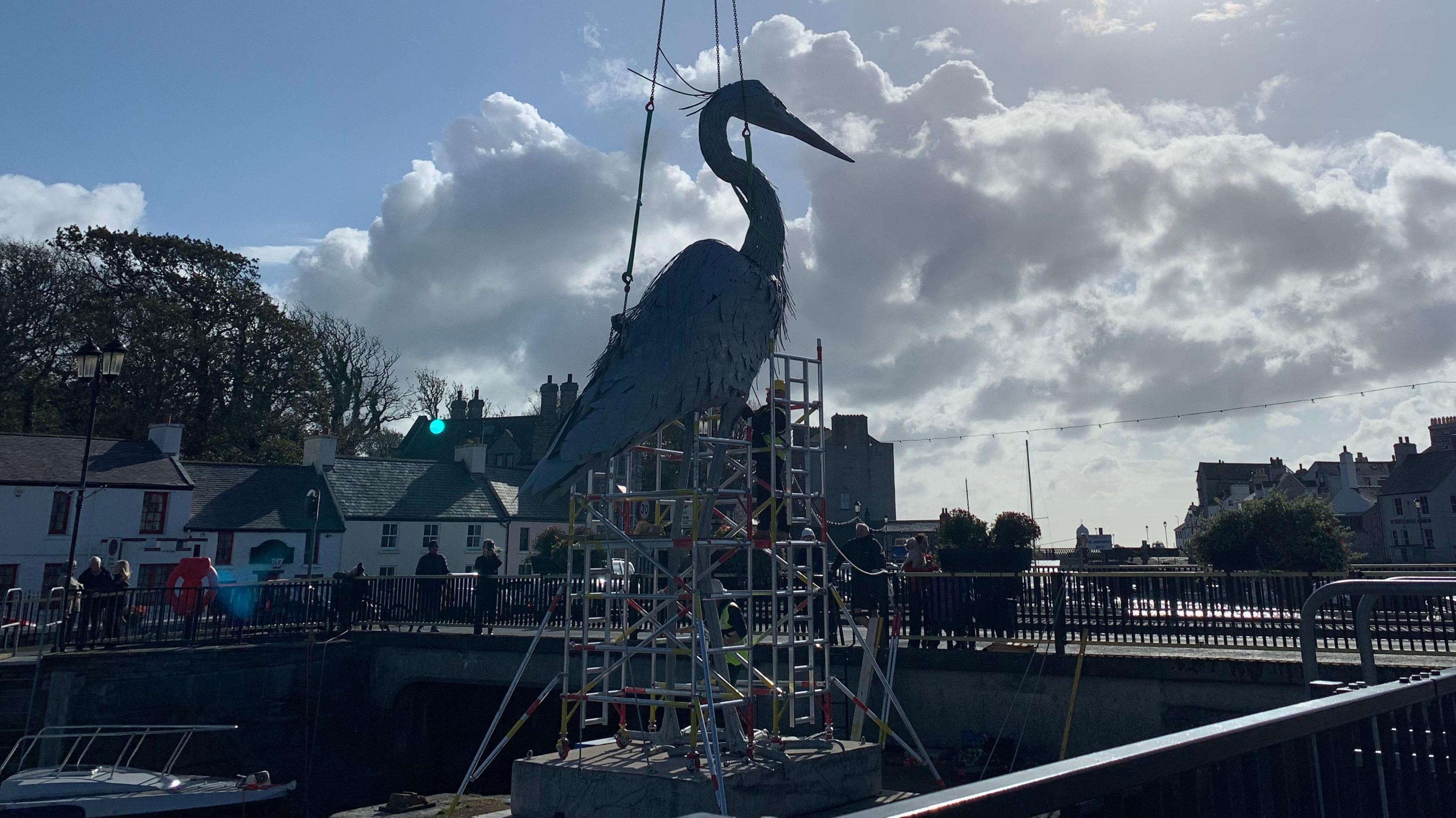 The giant heron sculpture being lowered onto the plinth which has  scaffolding around it.