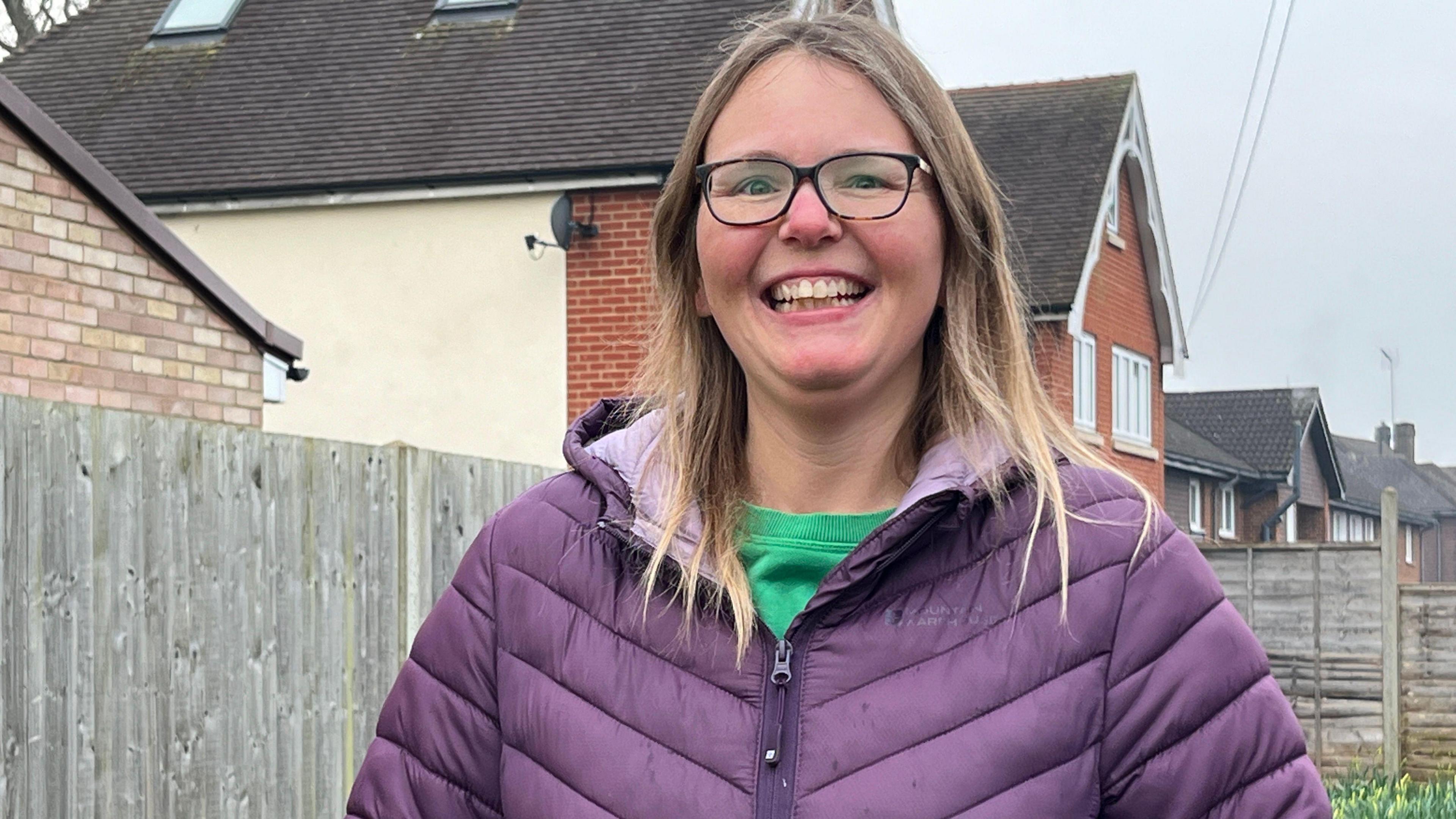 Close up shot of Annette Whymark smiling to camera standing against a fence with houses in the background