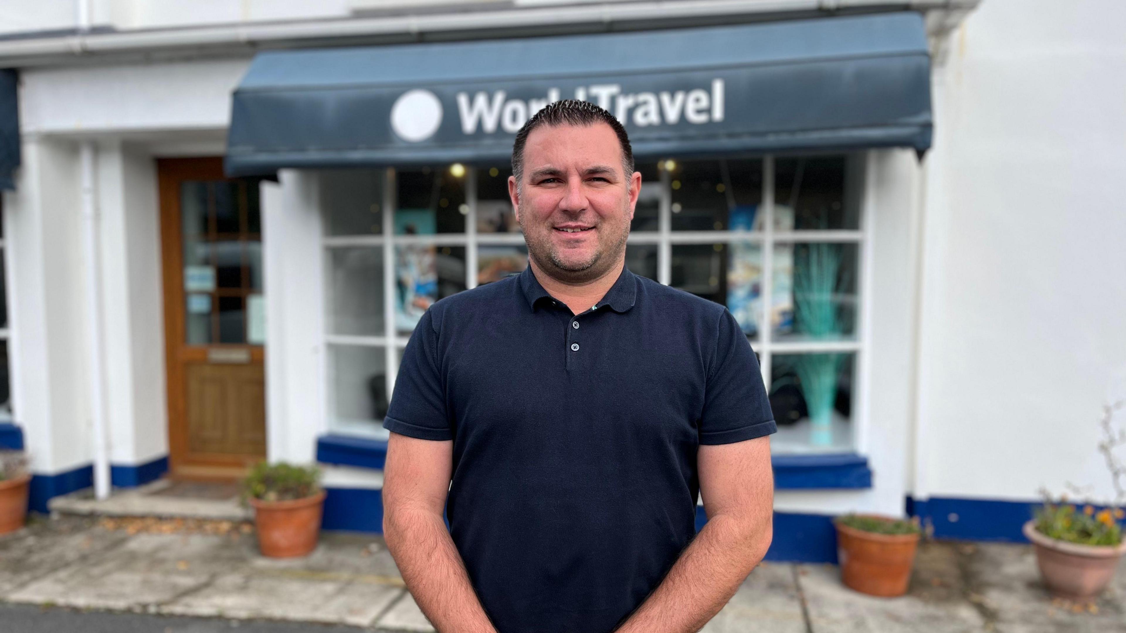 A man in a blue polo shirt outside a travel agent shop