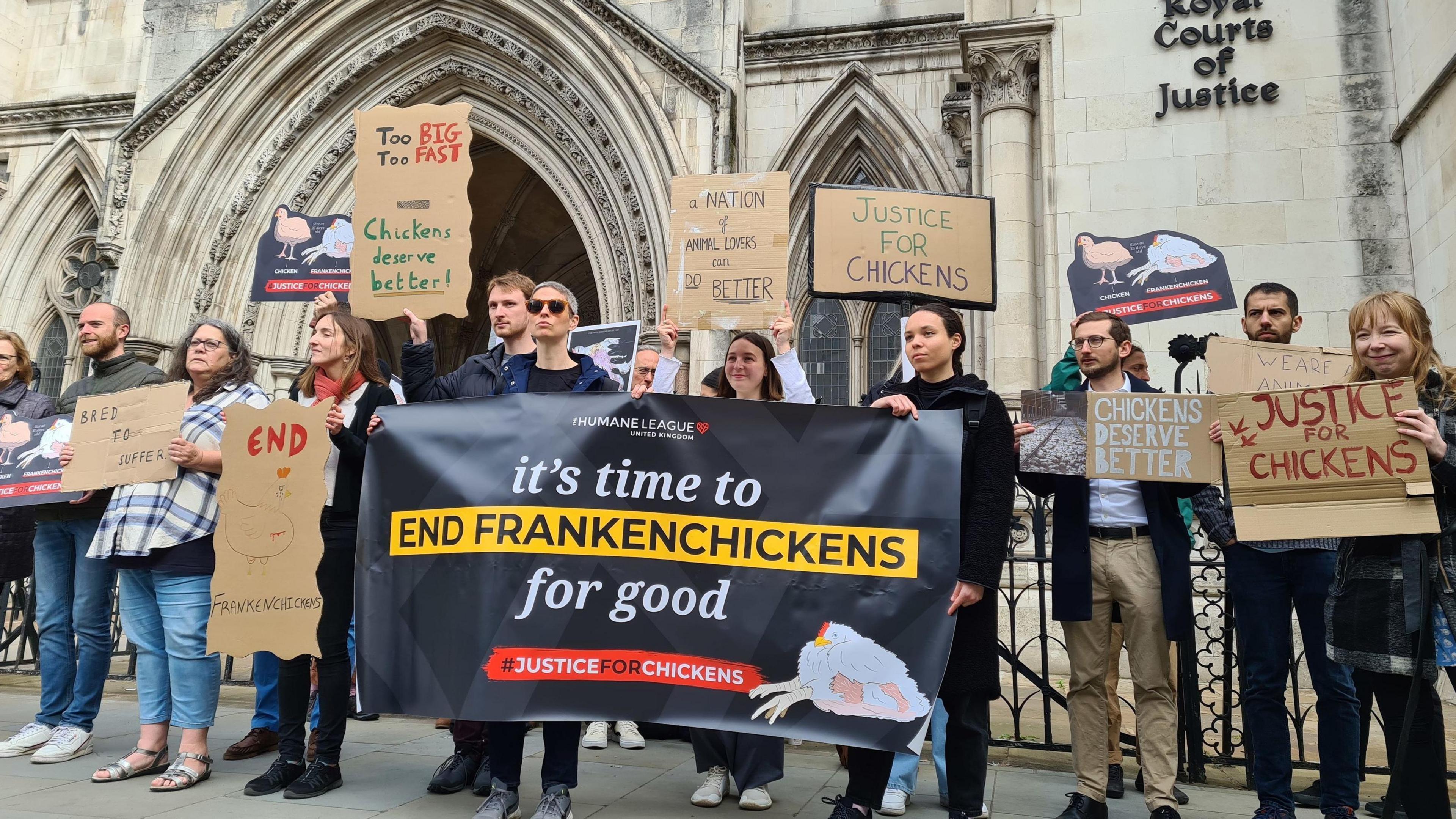 Campaigners stand outside of the Royal Court of Justice in London holding banners. One reads "it's time to end Frankenchickens for good".