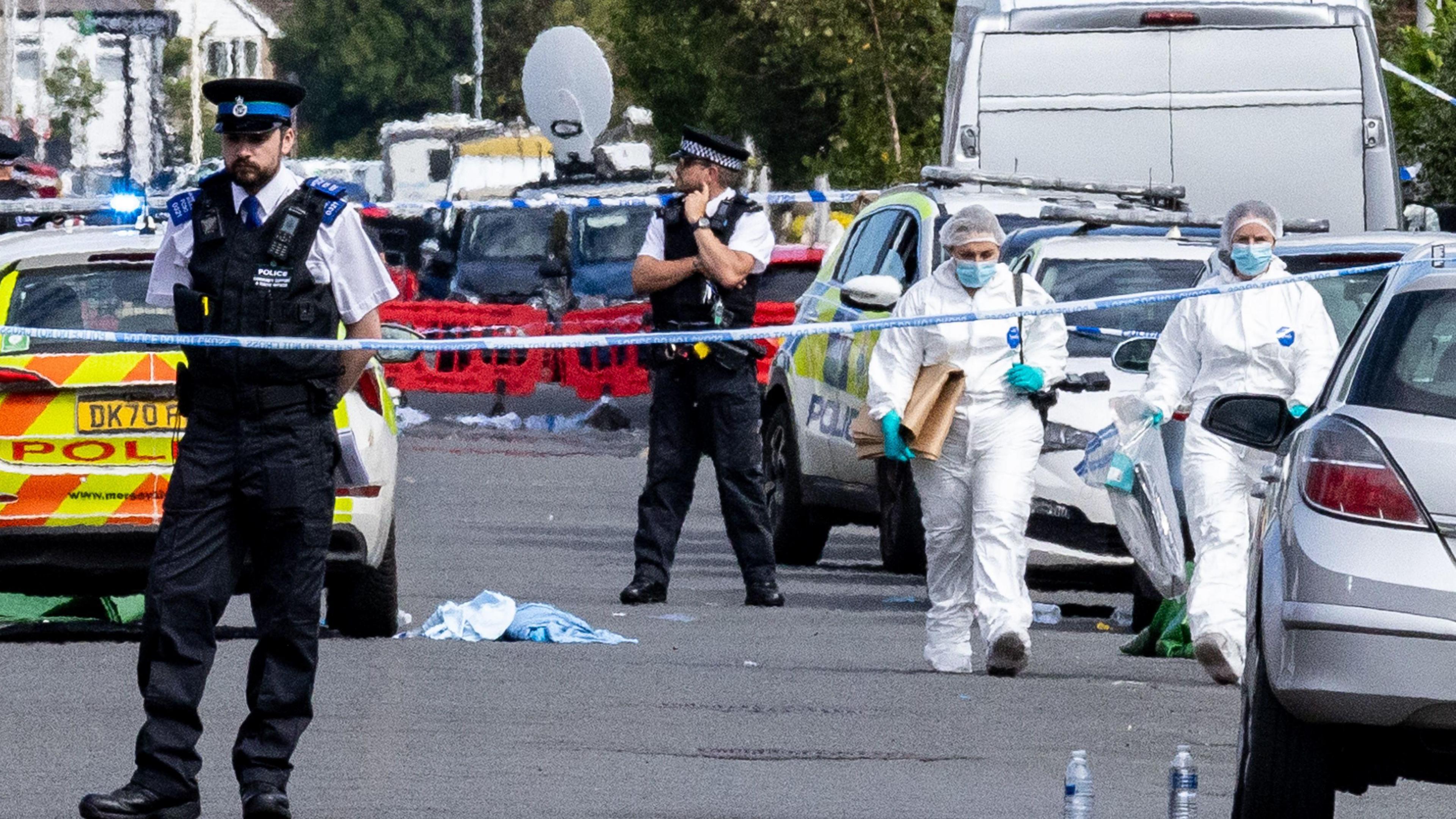Police and forensics on Hart Street Southport, Merseyside, after stabbings of children at a dance class. There is police tape cordoning off the road, several cars and two people in white suits 