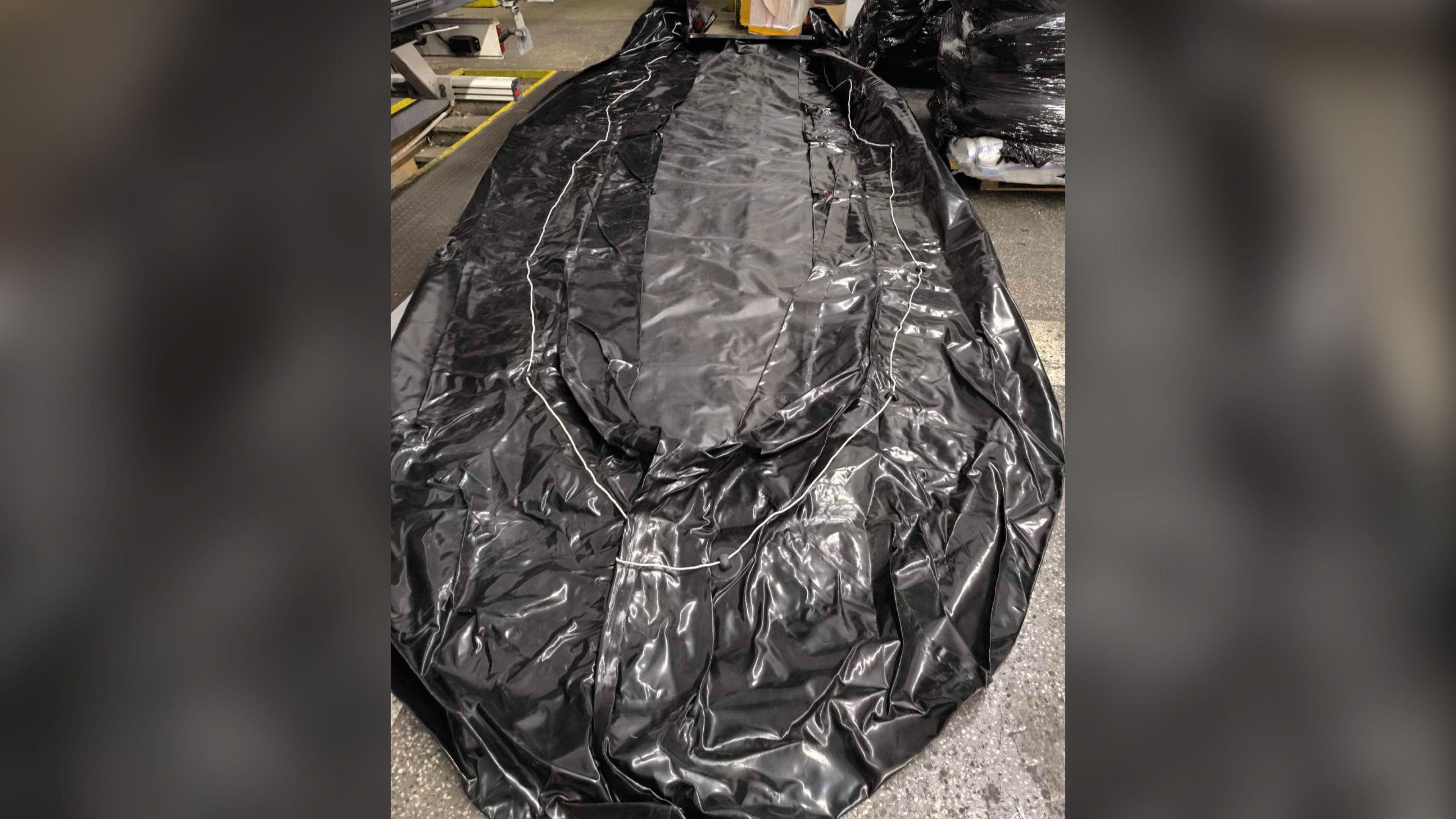 A rolled-out, deflated black boat.
