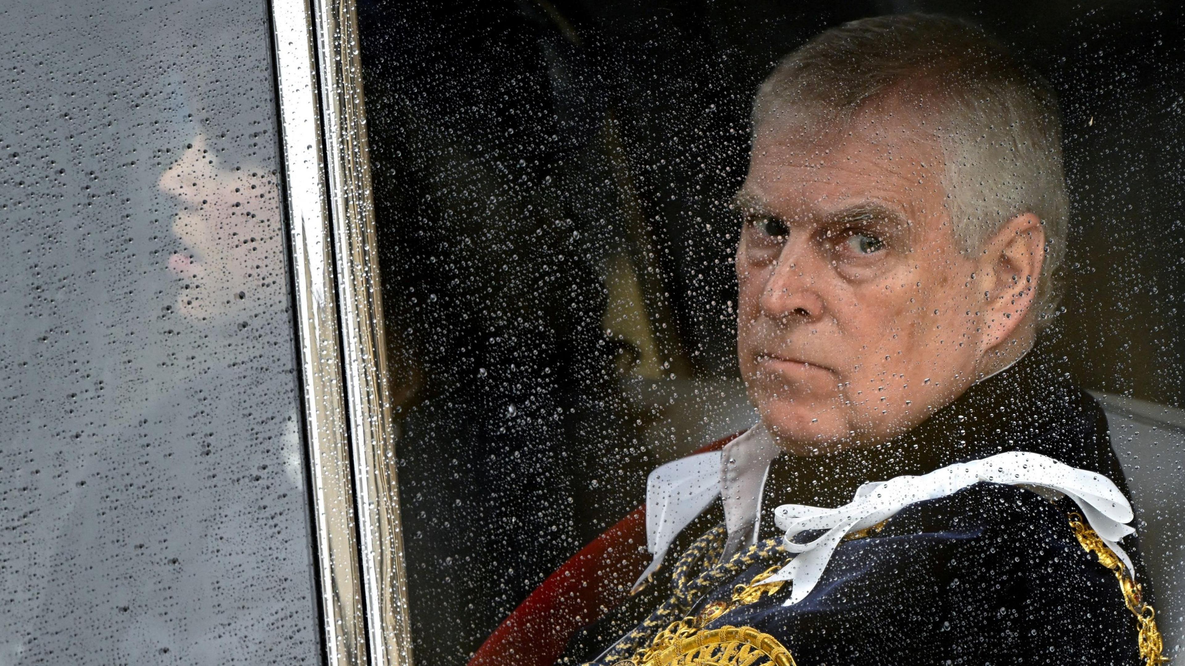 Prince Andrew looks out of the window of a vehicle. He has gold detailing on the clothing he is wearing.