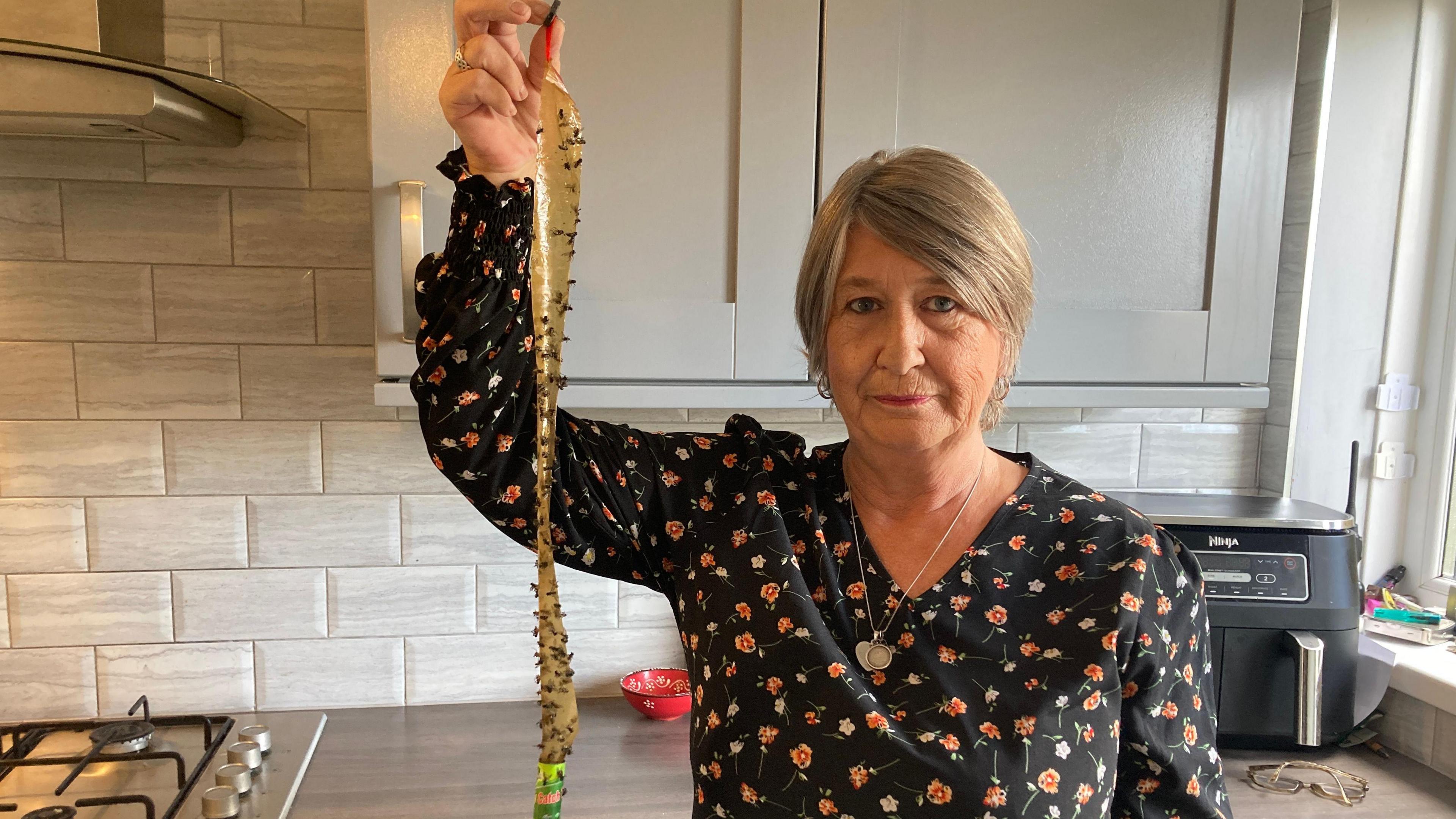 Picture of Geraldine Hooper holding up her fly papers covered in flies 