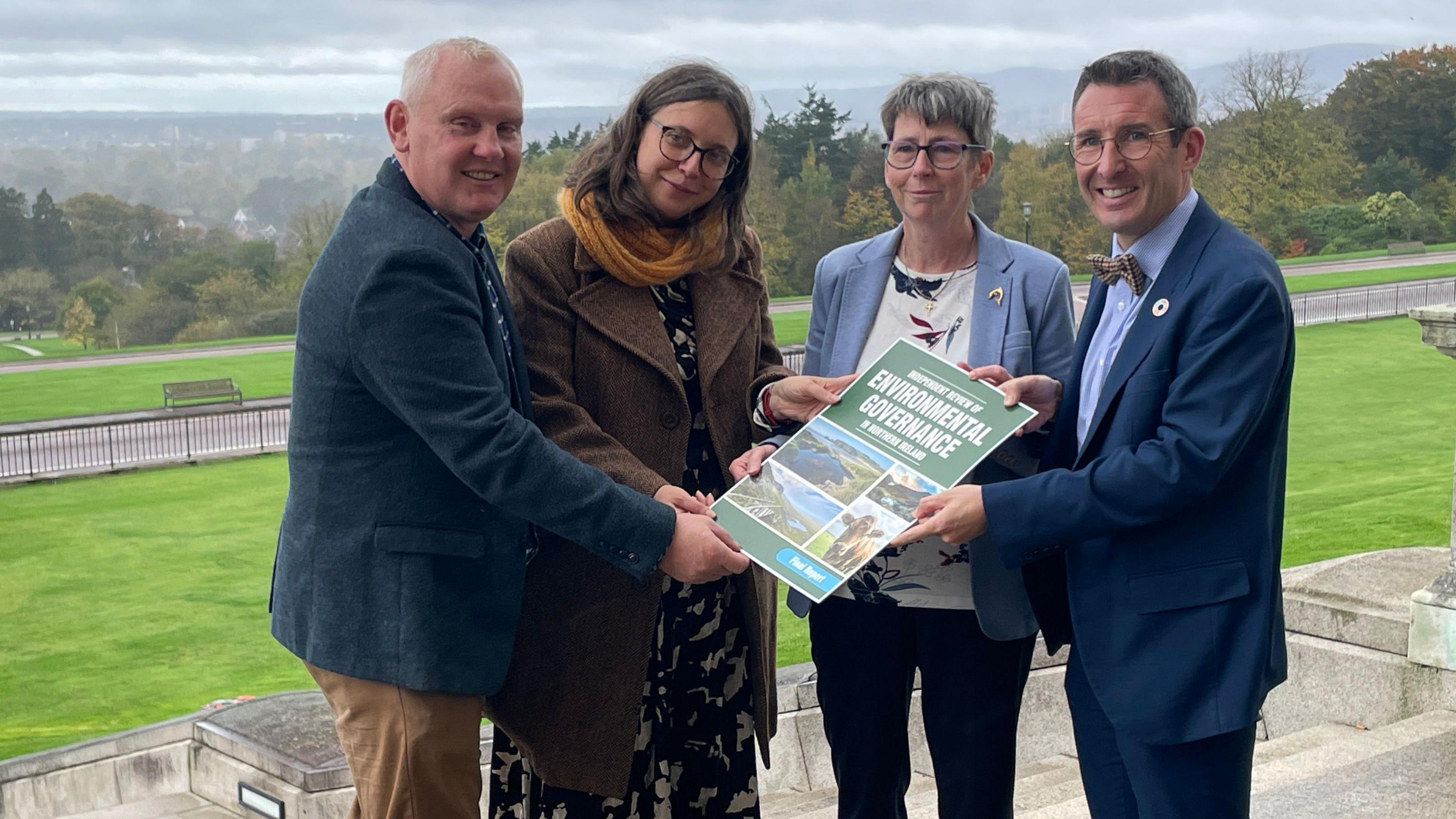 John McCallister, Dr Vivian Gravey, Diane Ruddock and Andrew Muir stand outside Stormont holding a booklet of the Environment Governance, which is green in colour.