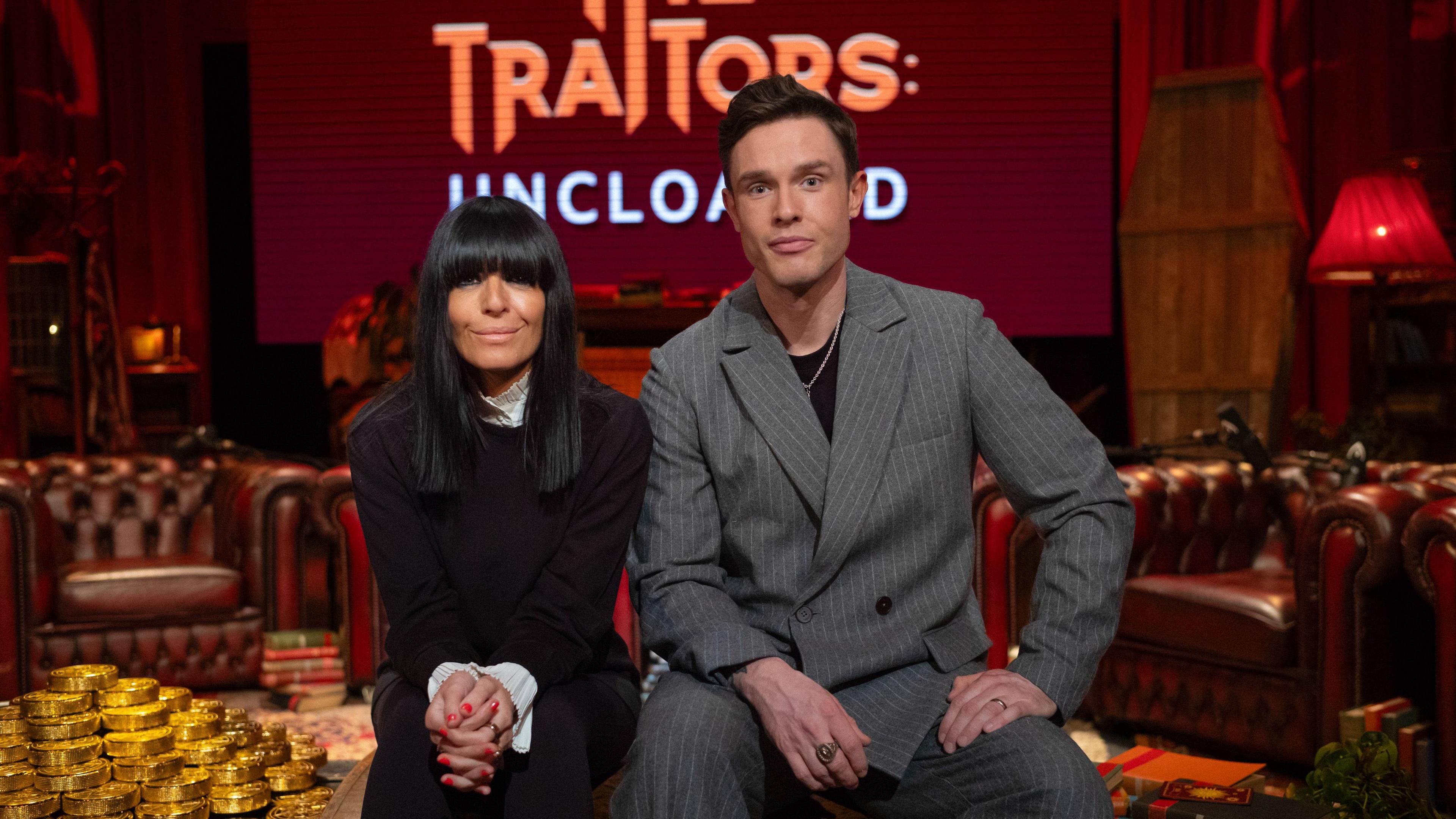 Claudia Winkleman wears all black as she sits next to Traitors: Uncloaked podcast host Ed Gamble, who wears a grey suit.
