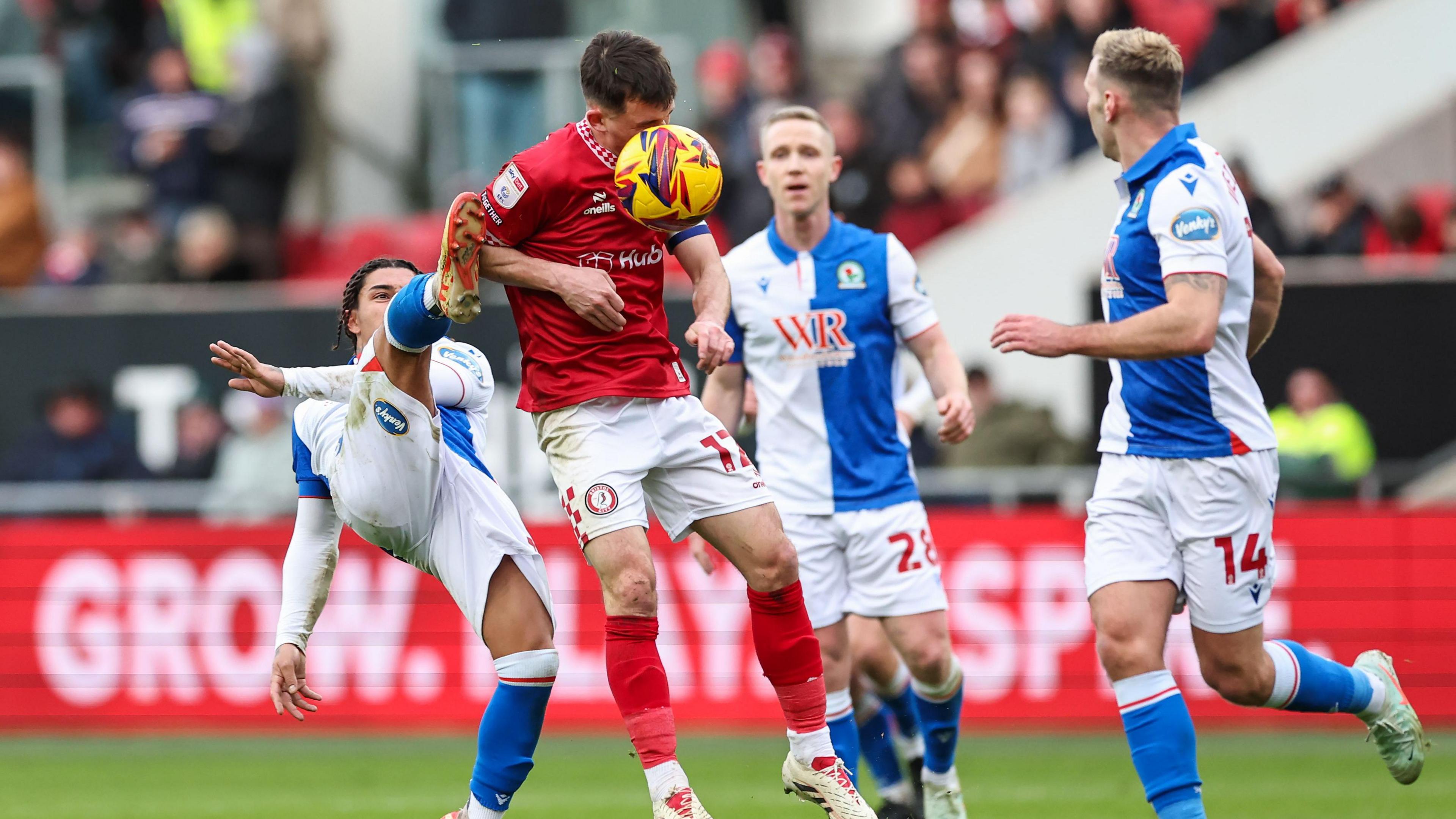 Bristol City and Blackburn Rovers players contest the ball during a Championship game at Ashton Gate. The Bristol City players are in their home kit of red shirts and socks and white shorts, while Blackburn are in their traditional blue and white shirts. Jason Knight, of Bristol City, is heading the ball as he is challenged