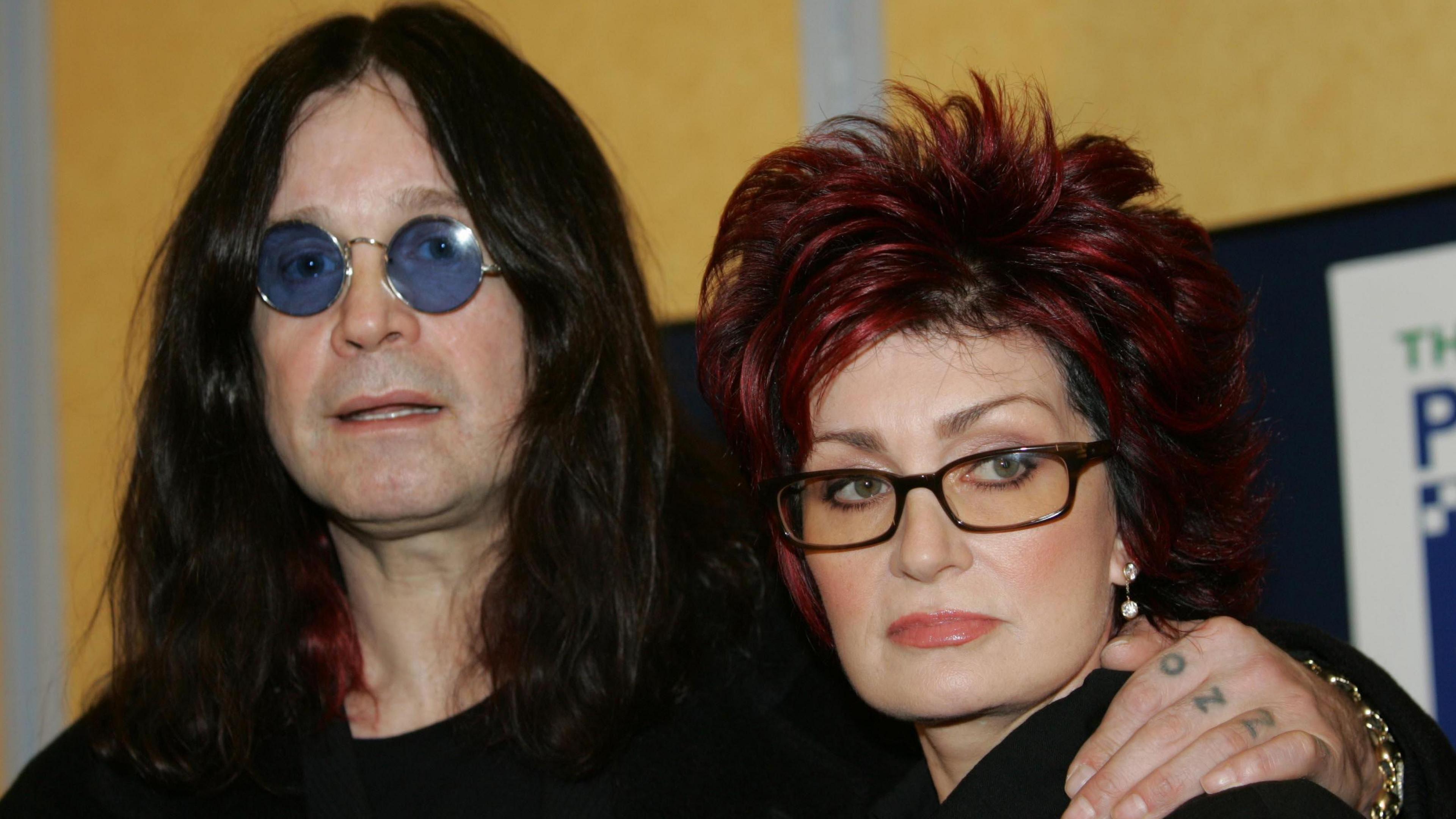 Ozzy Osbourne wearing sunglasses with his arm around wife Sharon's shoulder. 