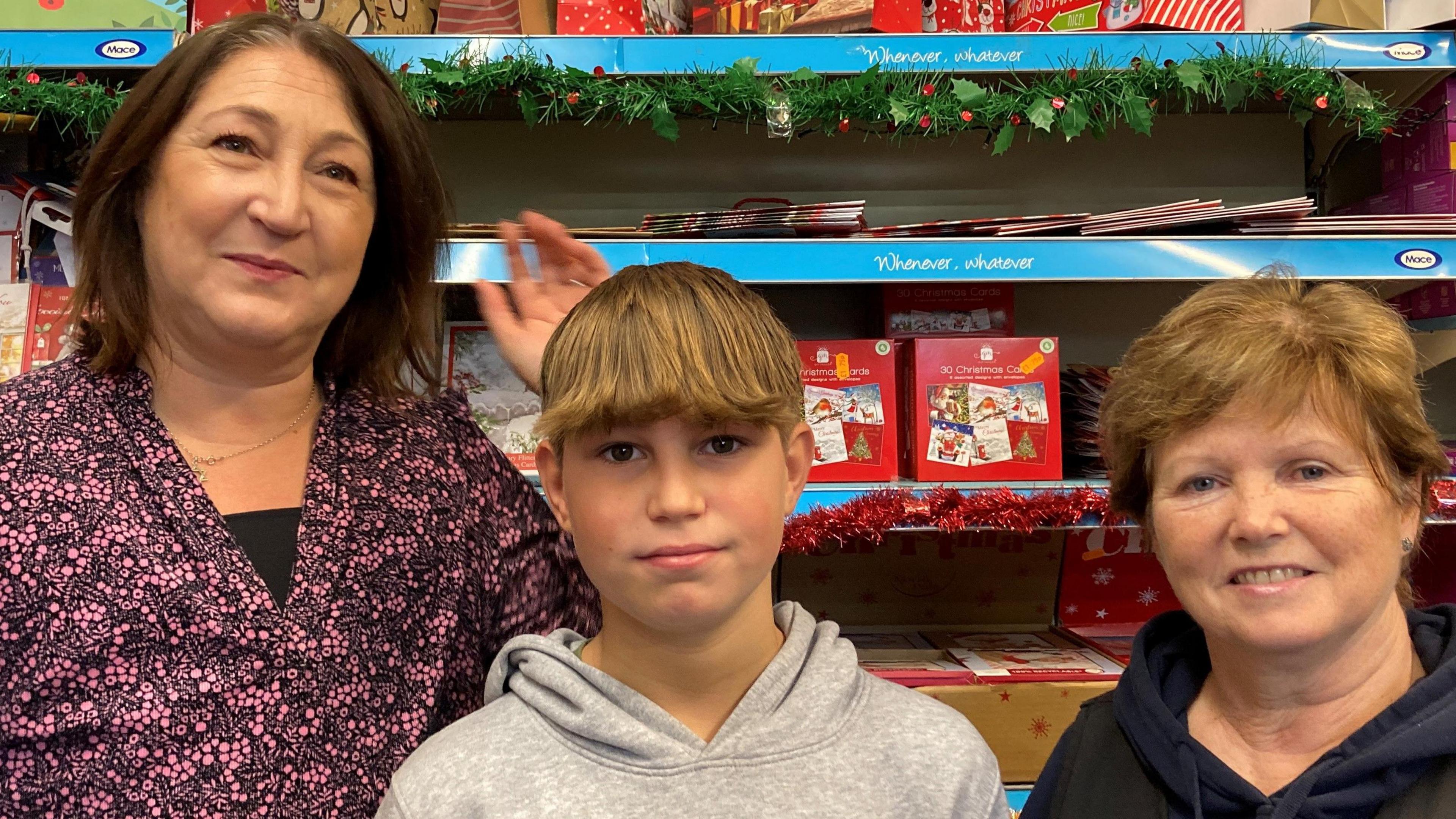 Ethan is in the centre of the photo with his mum Zoe on the left and shop manager Wendy Ellis on the right. They're standing in front of a shelf of Christmas cards.   