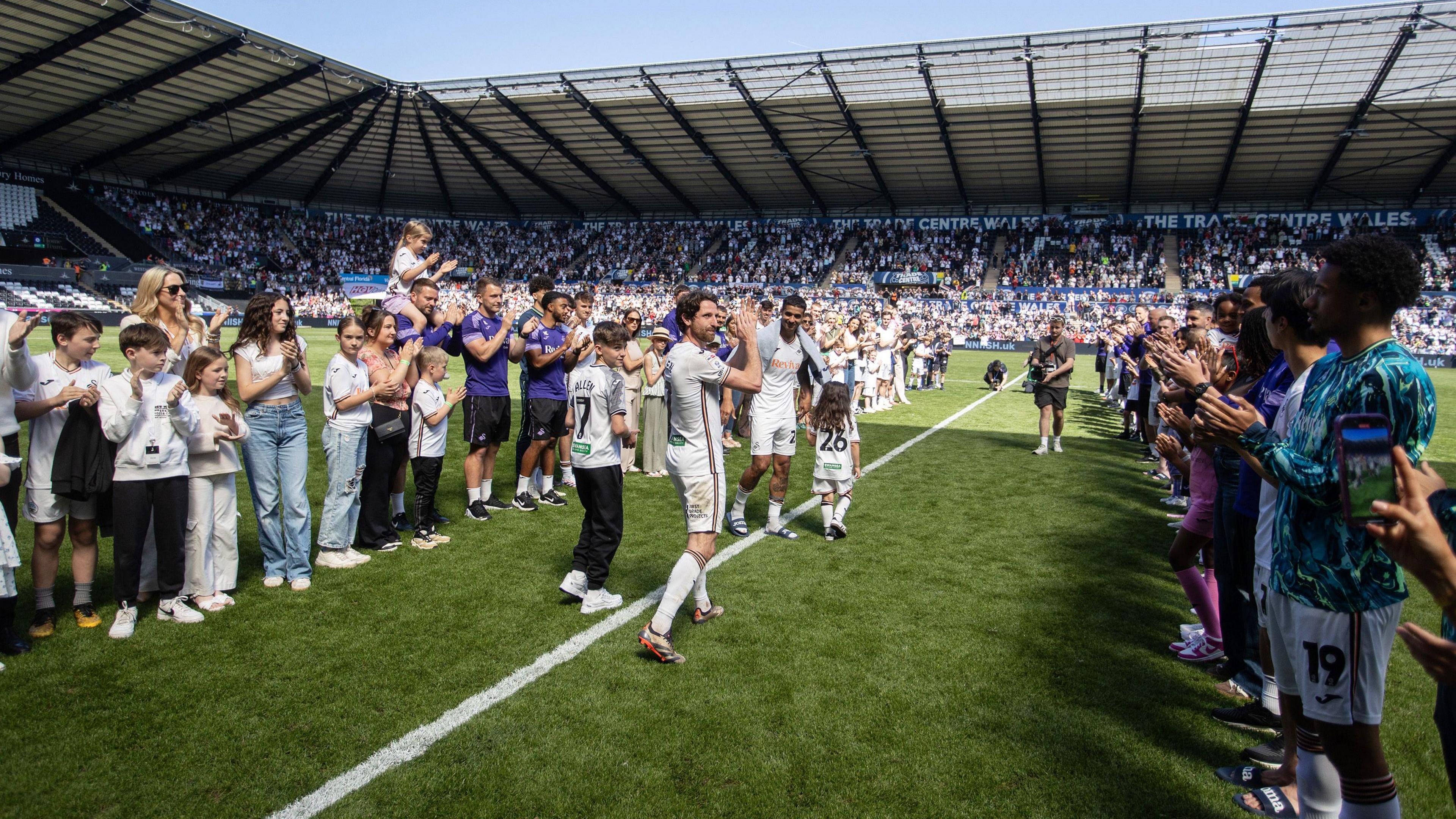 Joe Allen applauds as he walks between rows of people on a football pitch