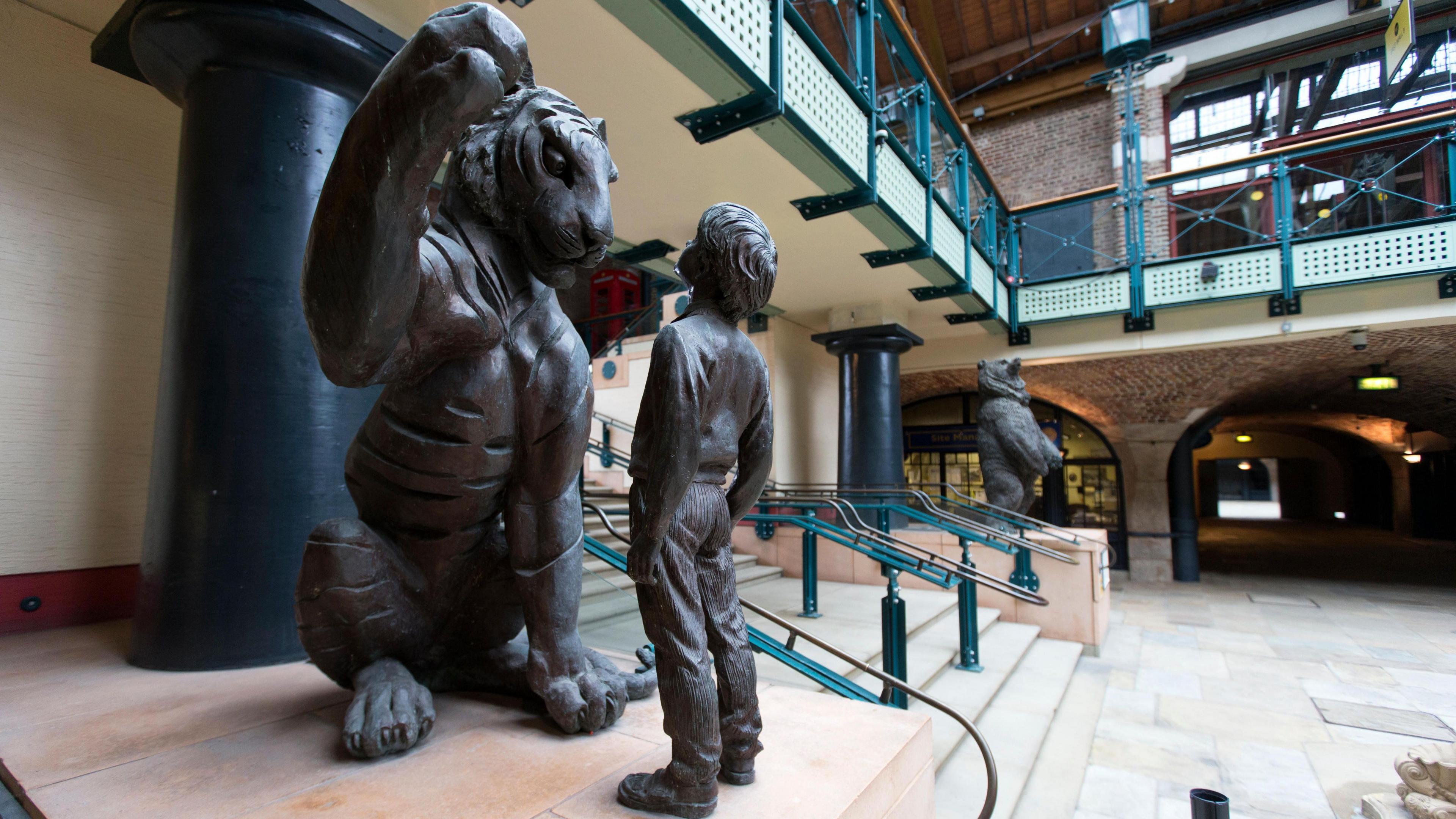 A large sculpture of a tiger sitting on it with one front paw in the air and a boy in front of it staring at its face