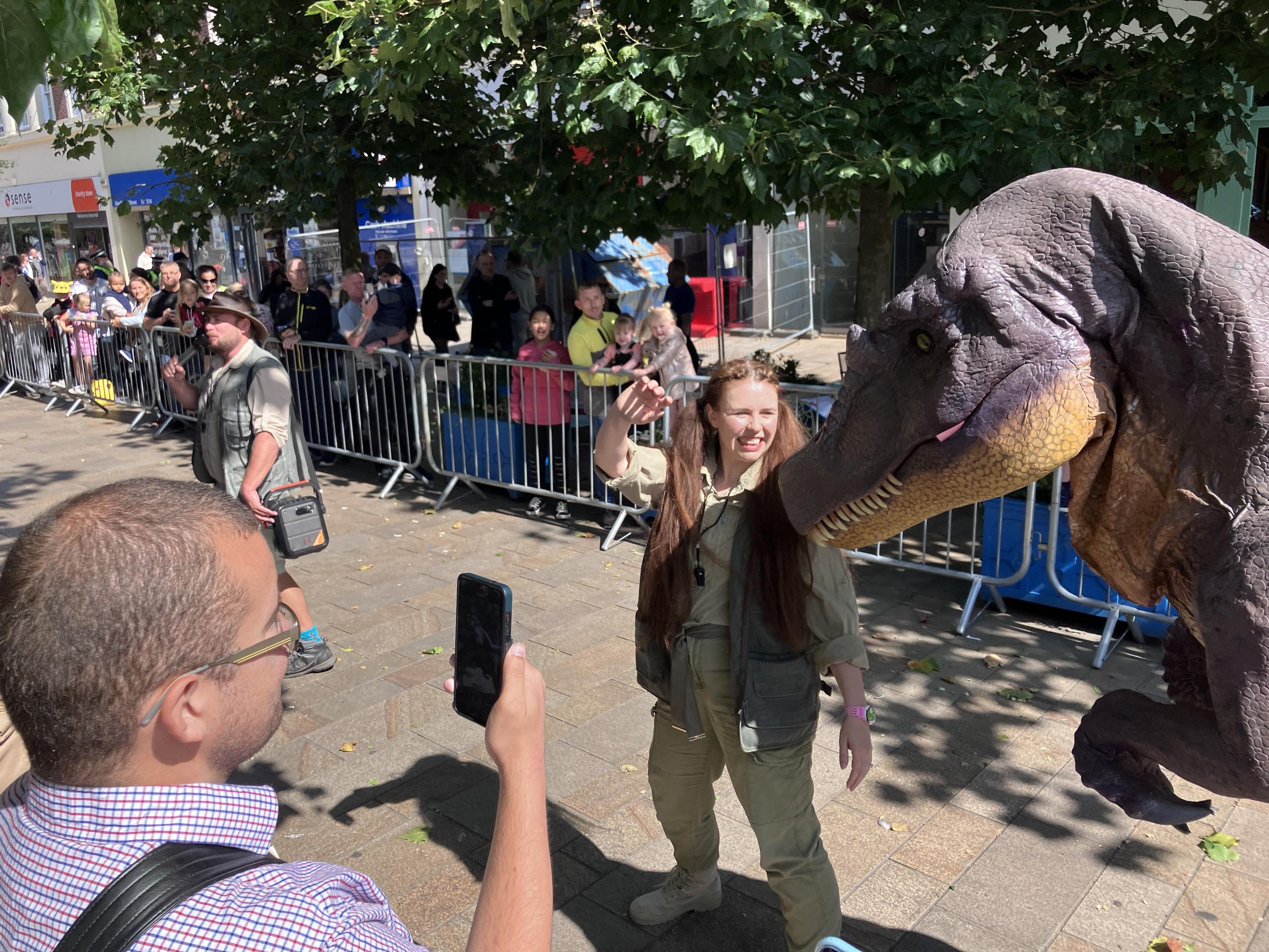 A man takes a photo of the dinosaur and park ranger