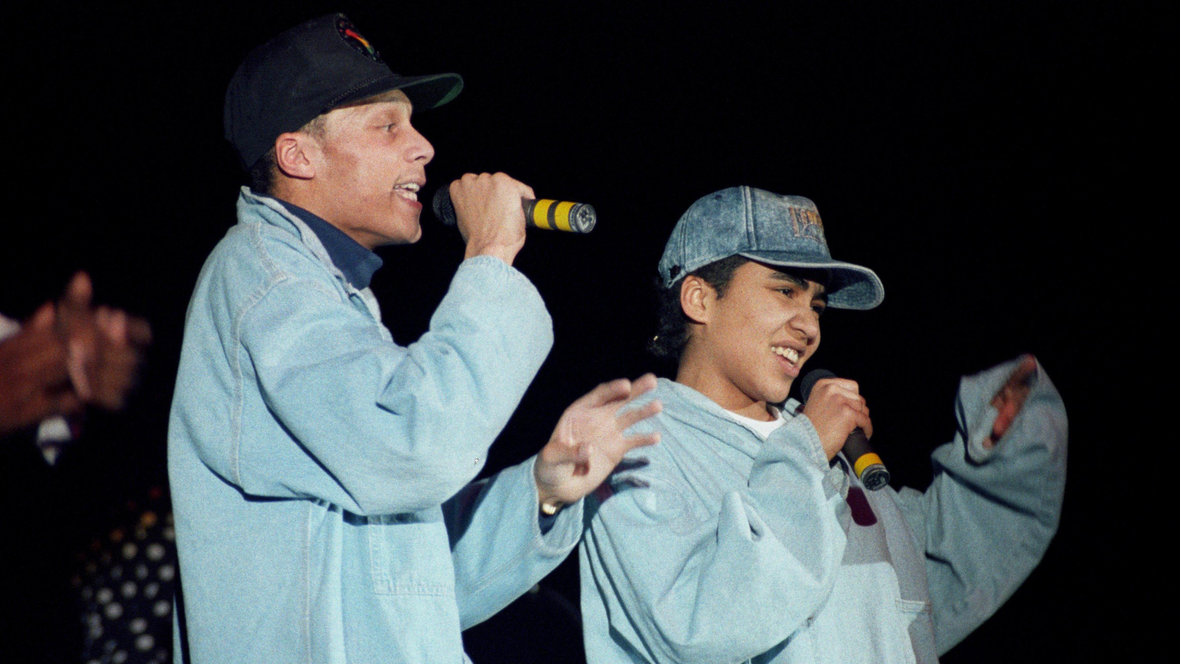 Two rappers, wearing grey, performing a tune to a crowd of fans.