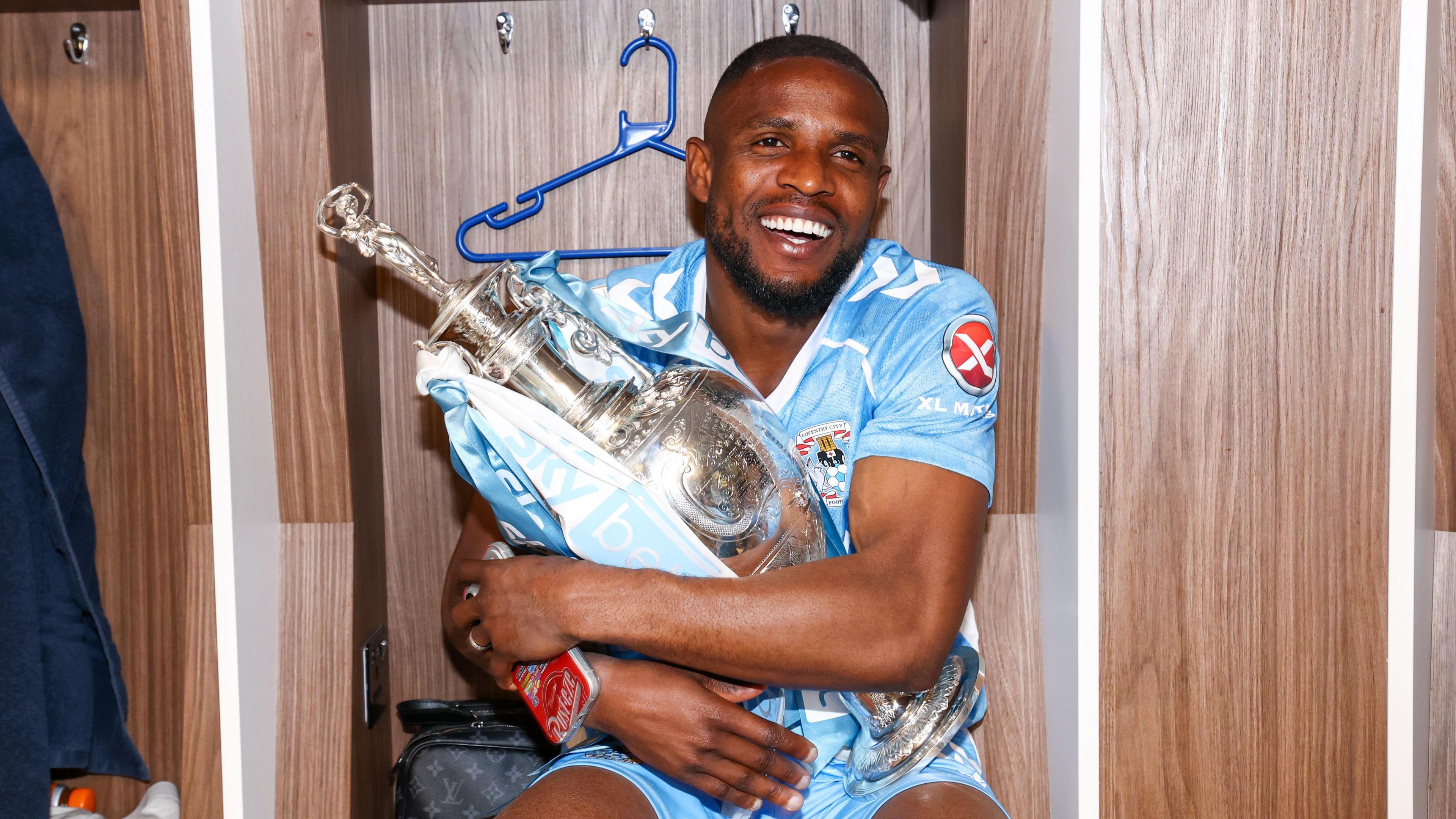 Frank Onyeka cuddles the Championship winners trophy in the dressing room after Coventry City's final game of the season