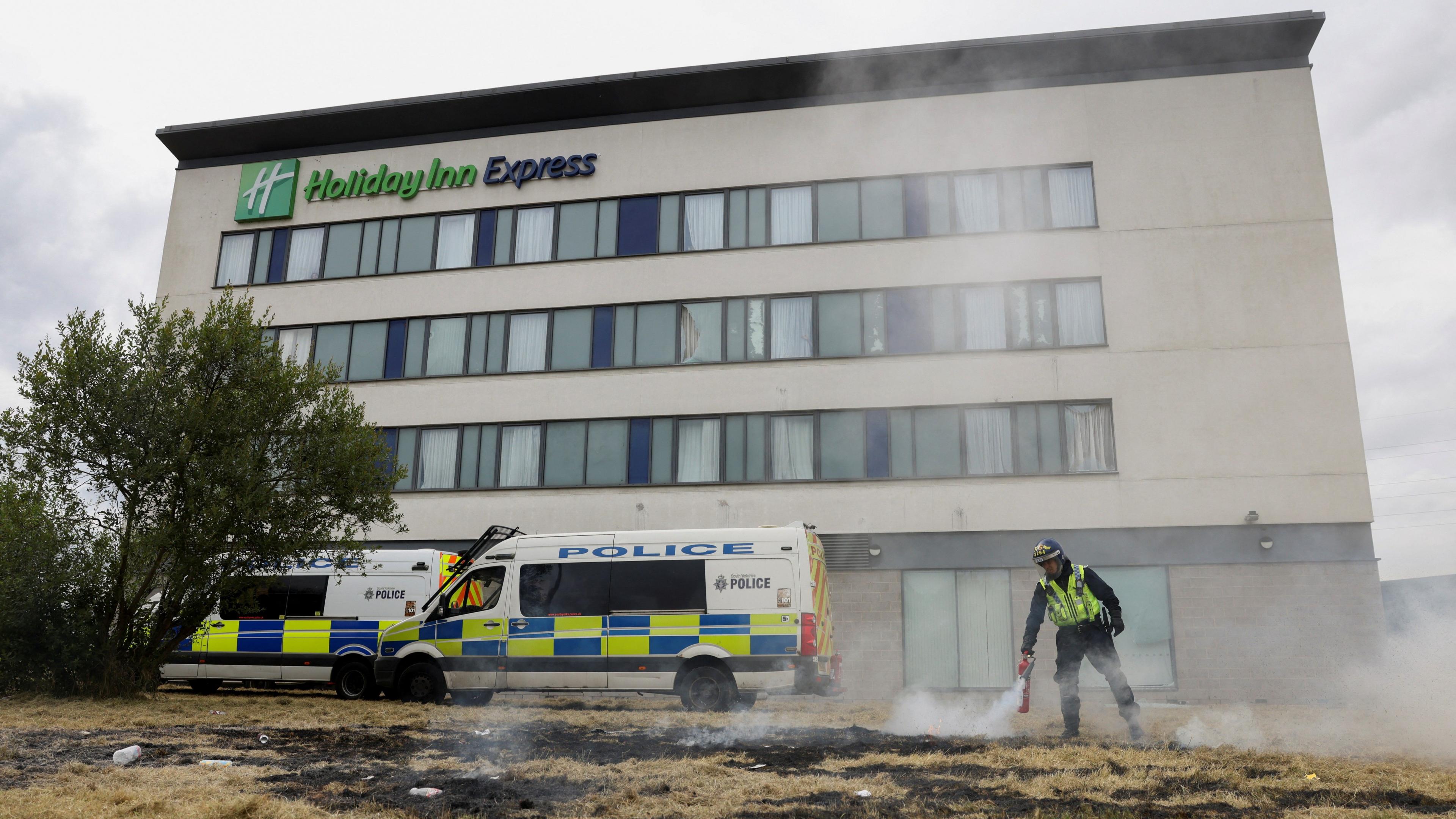 a police officer and two police vans outside the Holiday Inn Express