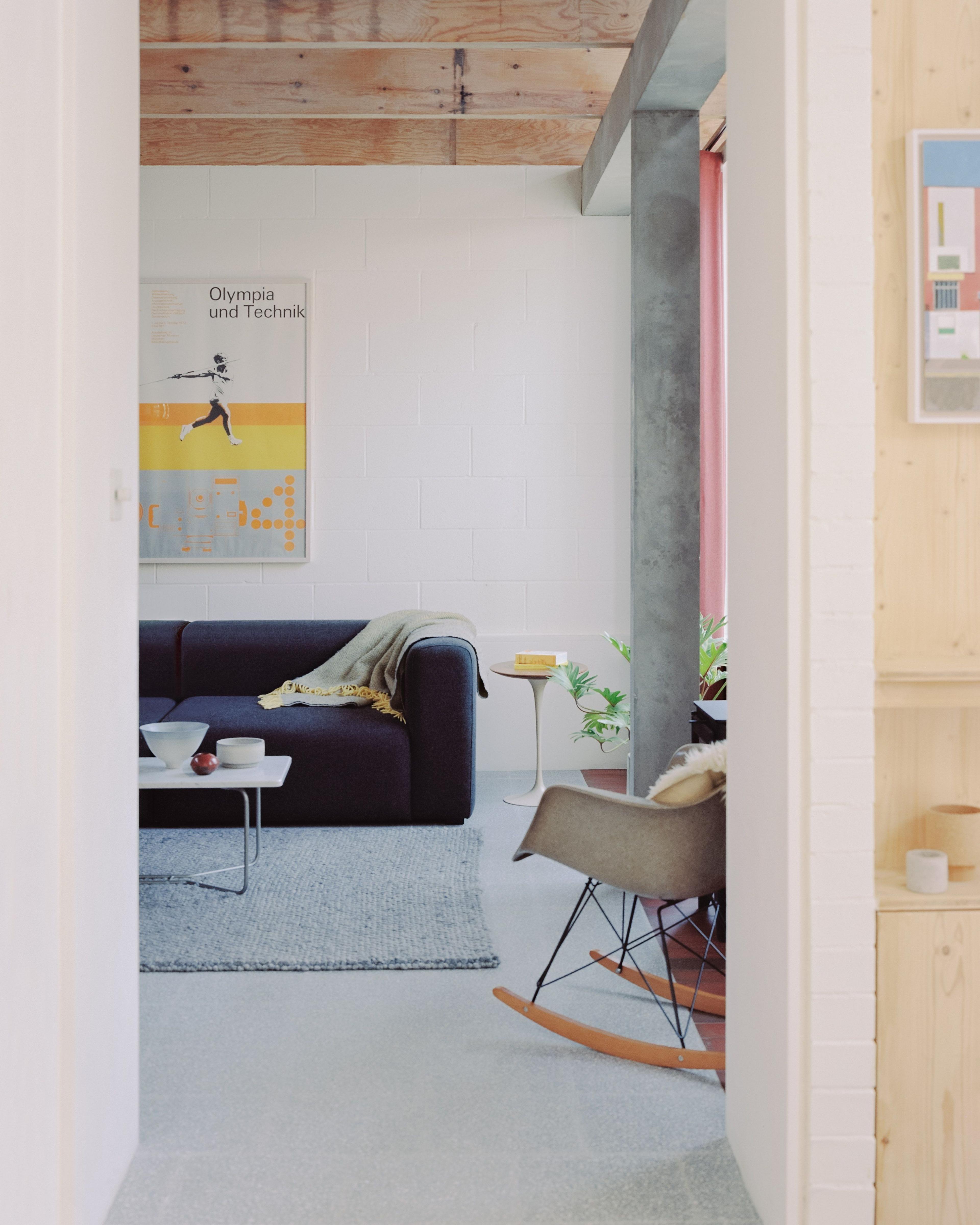 A view into the living room from a corridor, showing a navy sofa against the far wall, and a partial view of a rocking chair on the right hand side.