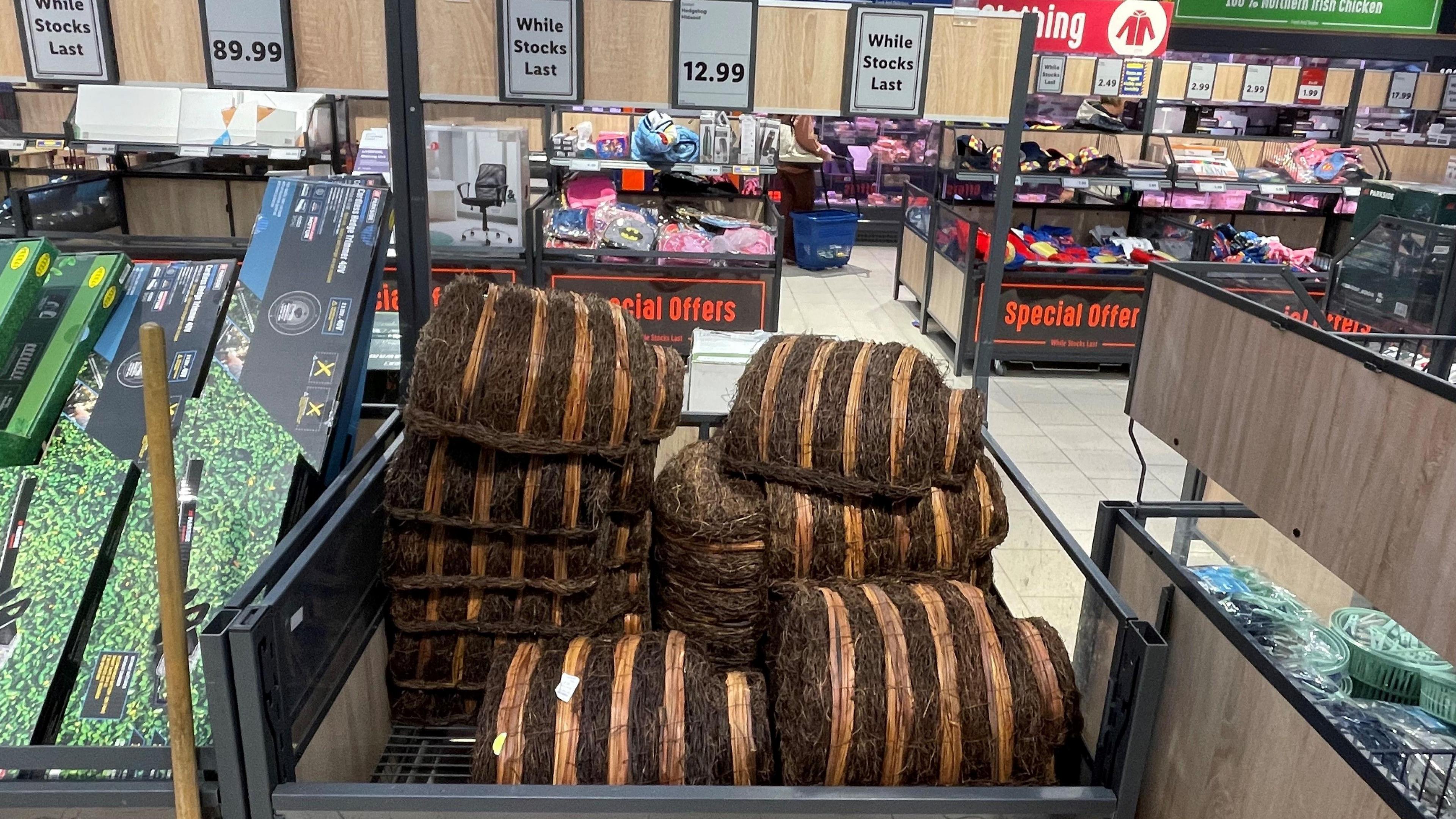 Hedgehog huts sitting on top of each other on display in a store. There is a sign above them saying "while stocks last!"