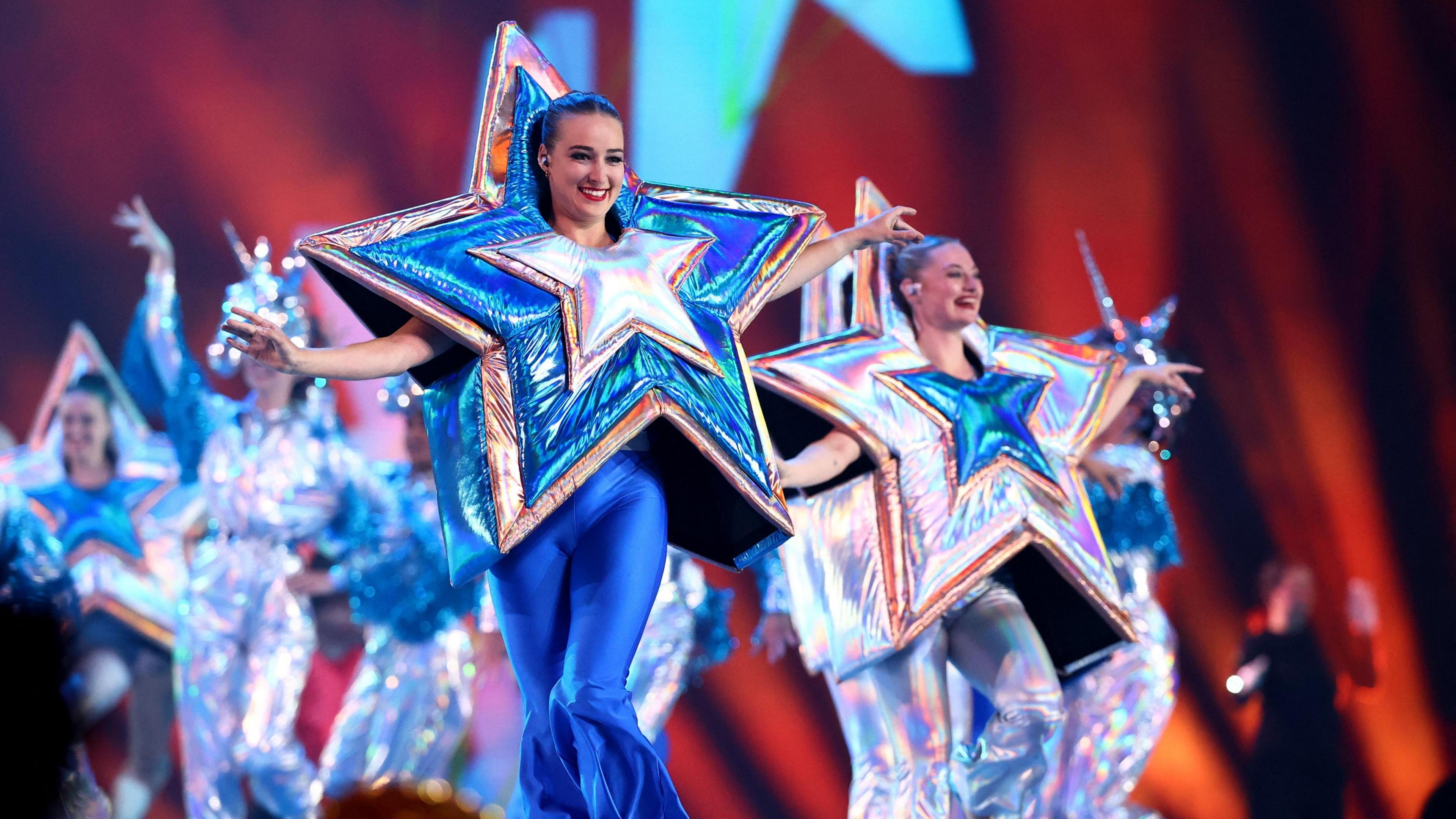 Dancers in big glitter, blue and silver star costumes dance on stage with bright lights.