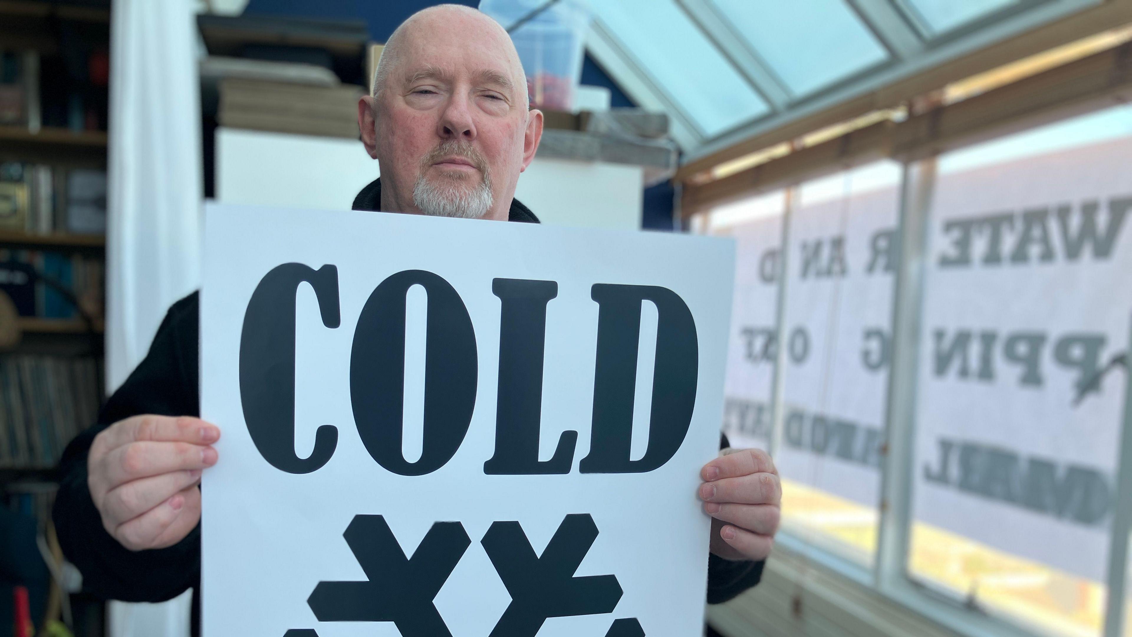 Patriic Gayle holding a large sign that reads: COLD with a snowflake underneath.
