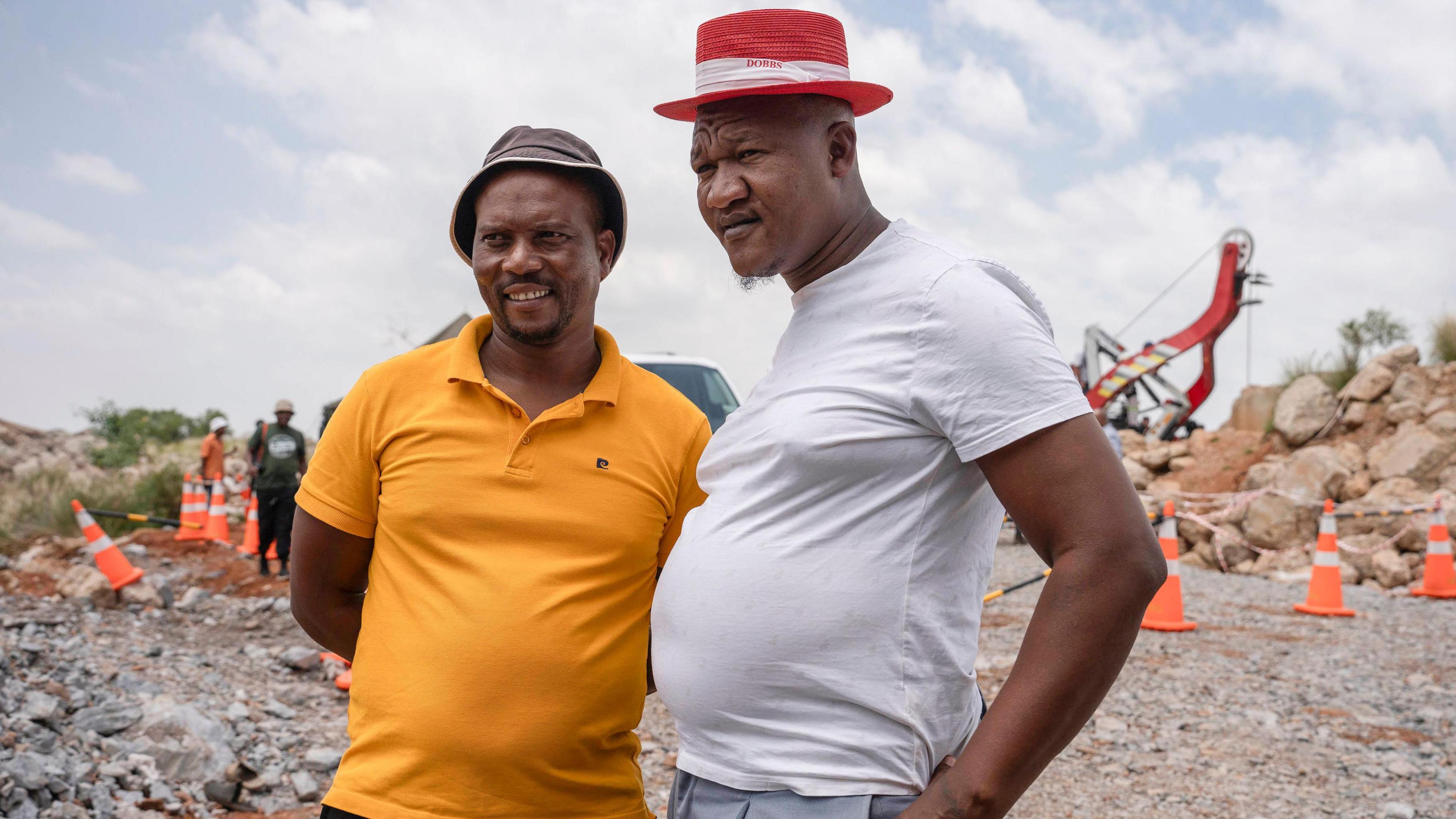 Mandla Charles and Mzwandile Mkwayi, the two community volunteers who descended into the abandoned mine, stand side by side near the top of the mine shaft. The one on the left is wearing a yellow T-shirt and the other is wearing a white T-shirt.