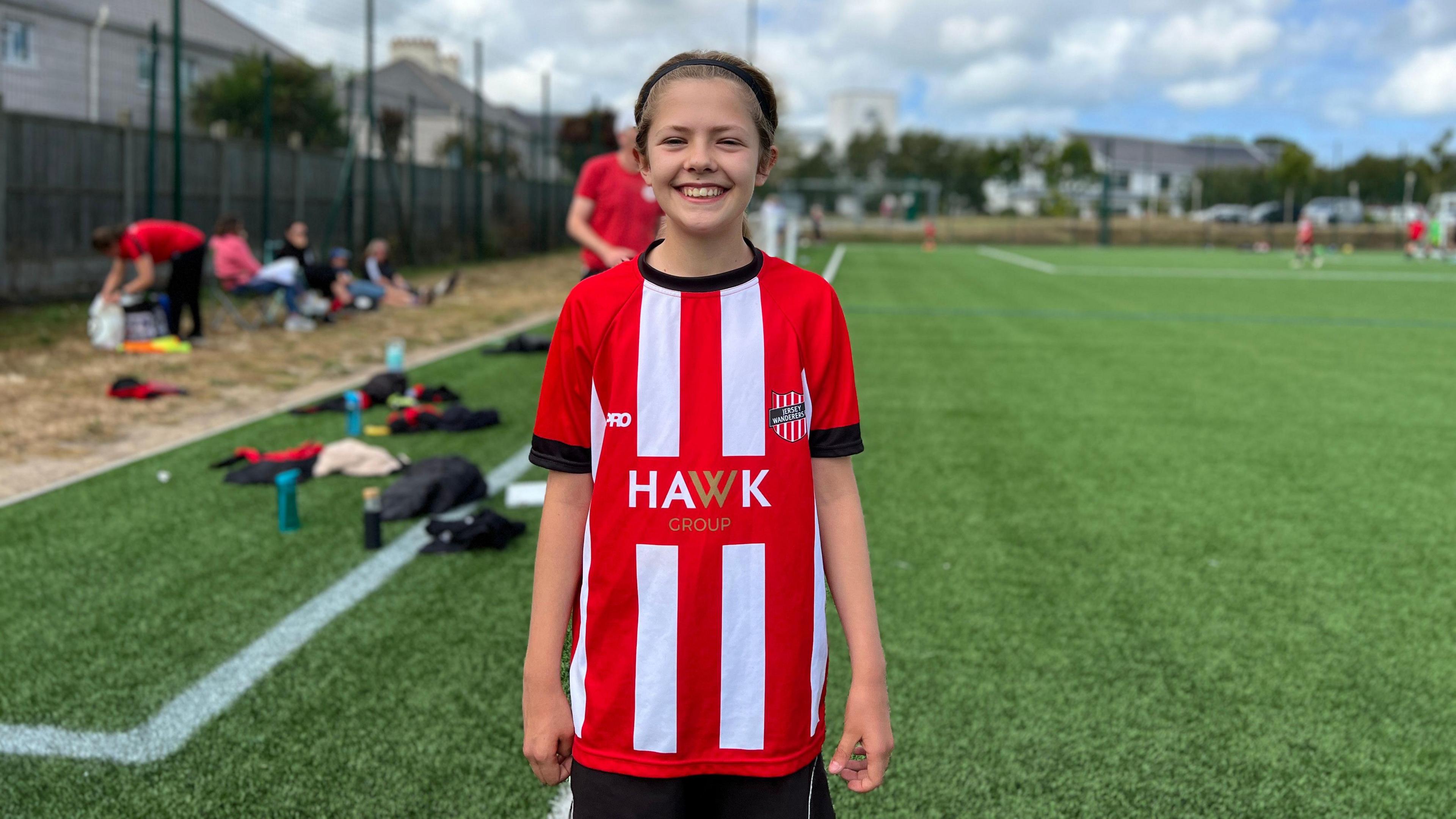 Anika smiles at the camera as she stands on a 4G pitch in her football kit