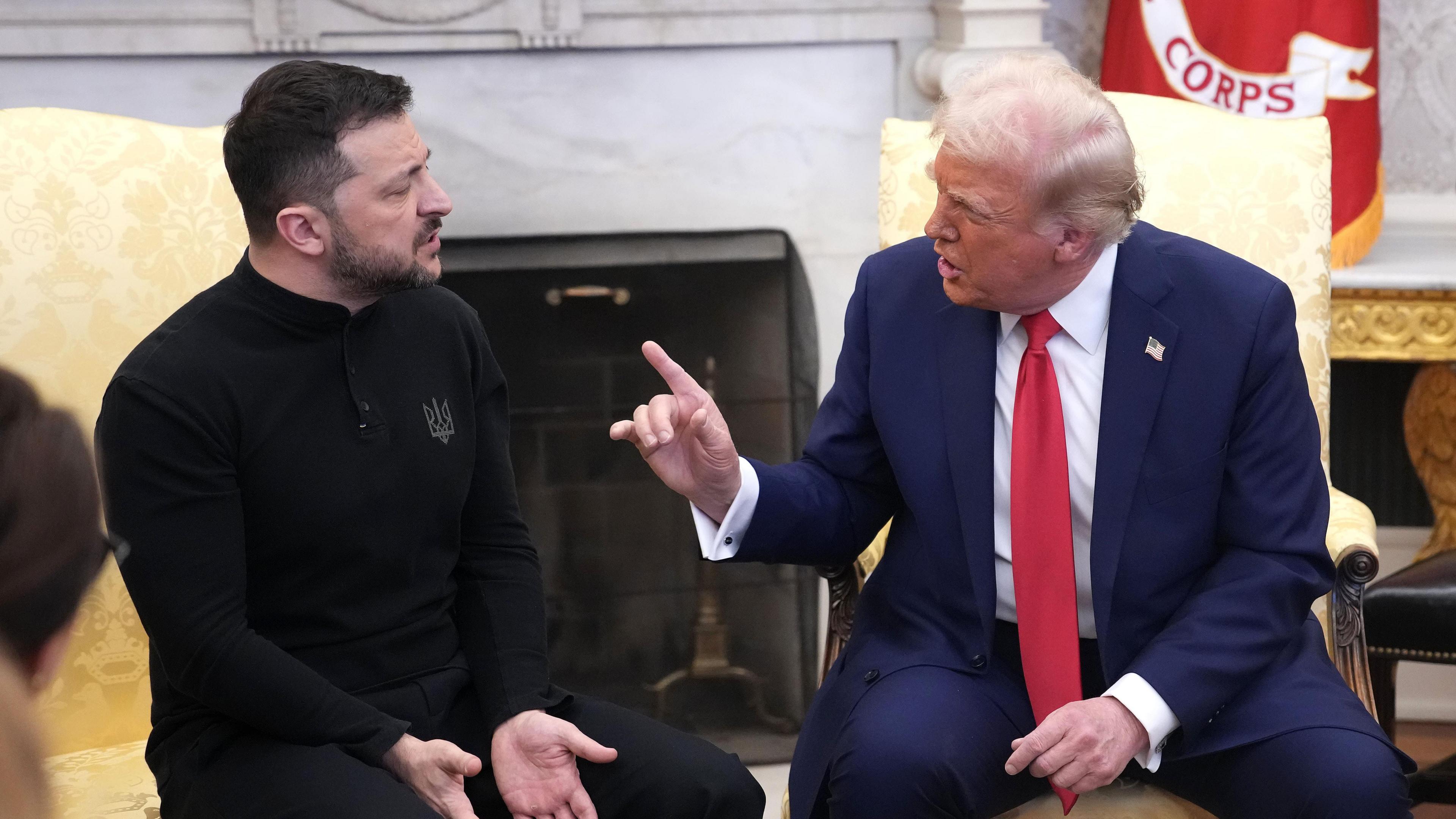 Zelensky and Trump face each other seated in the White House. Zelensky, dressed in black, has his hands down, while Trump, in a suit with red tie, raises his right hand and forefinger.