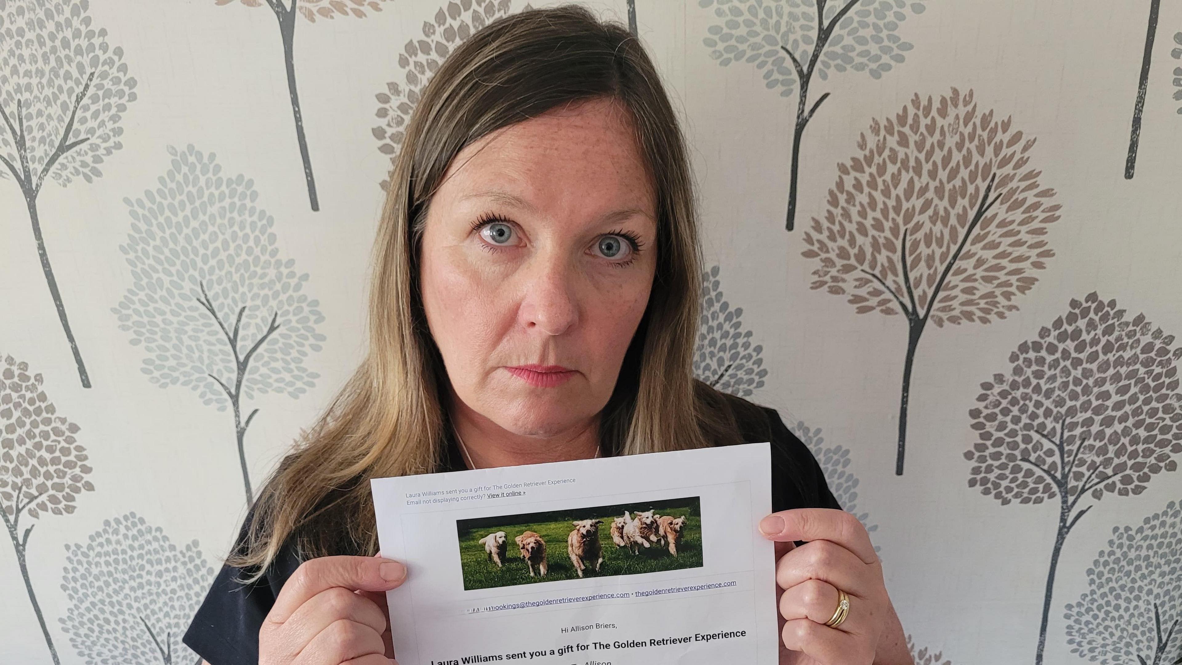 Women with long hair. She's looking sad to the camera. She's holding an A4 paper document with a voucher with dogs running around 