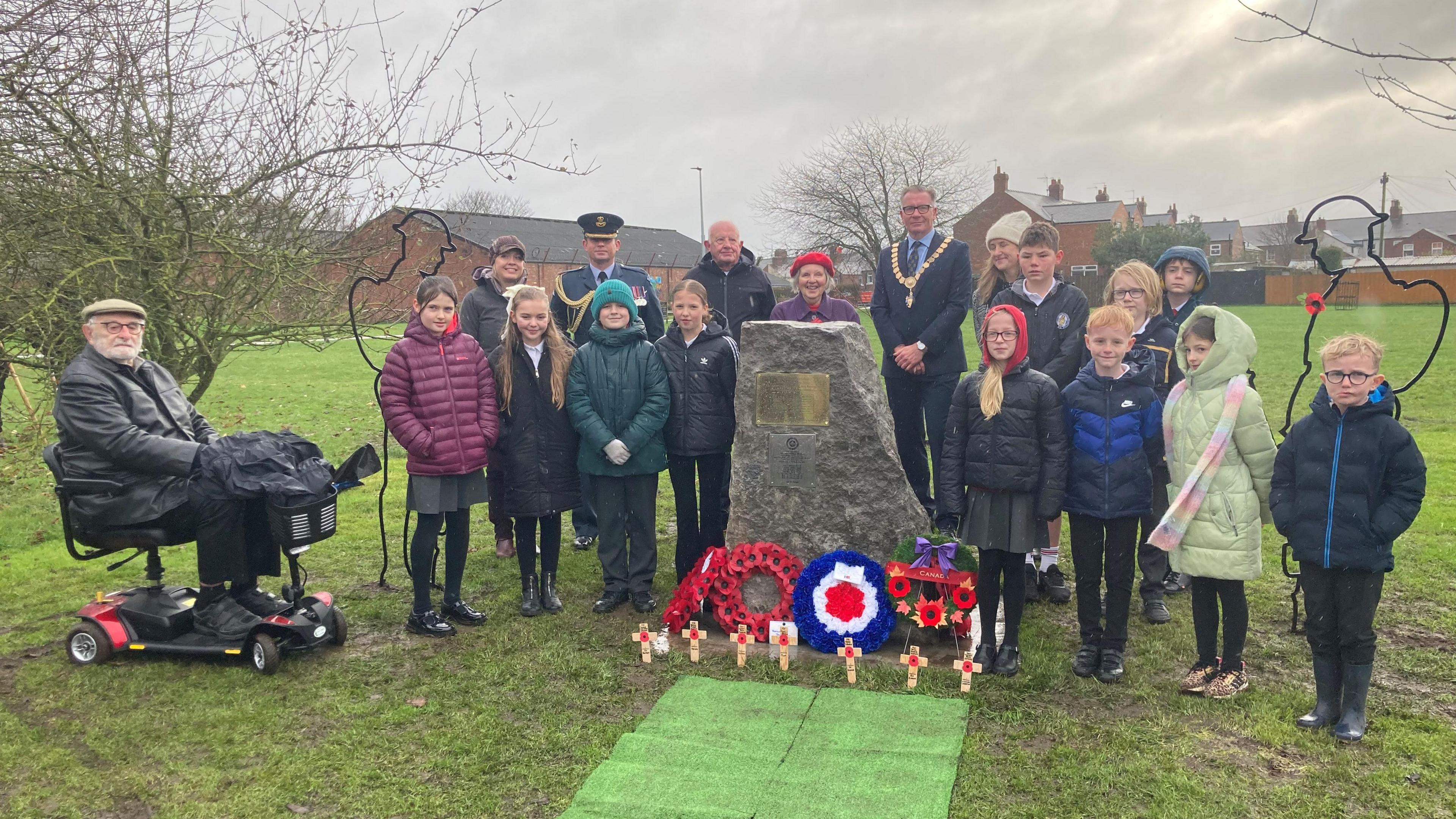 Mayor, pupils, former pupil and survivor with the memorial stone, which has floral tributes in front of it