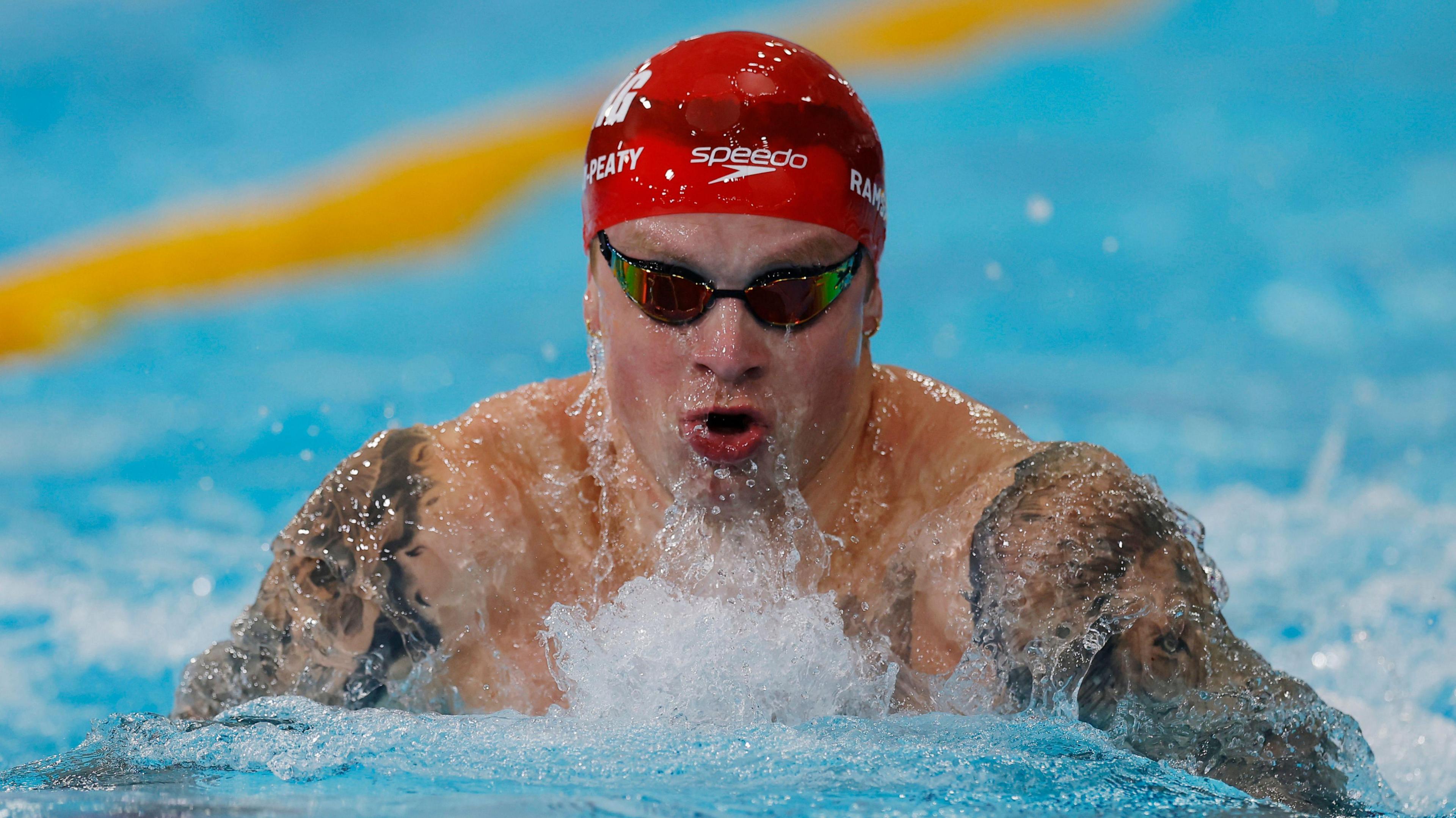 Adam Peaty swimming wearing a red cap